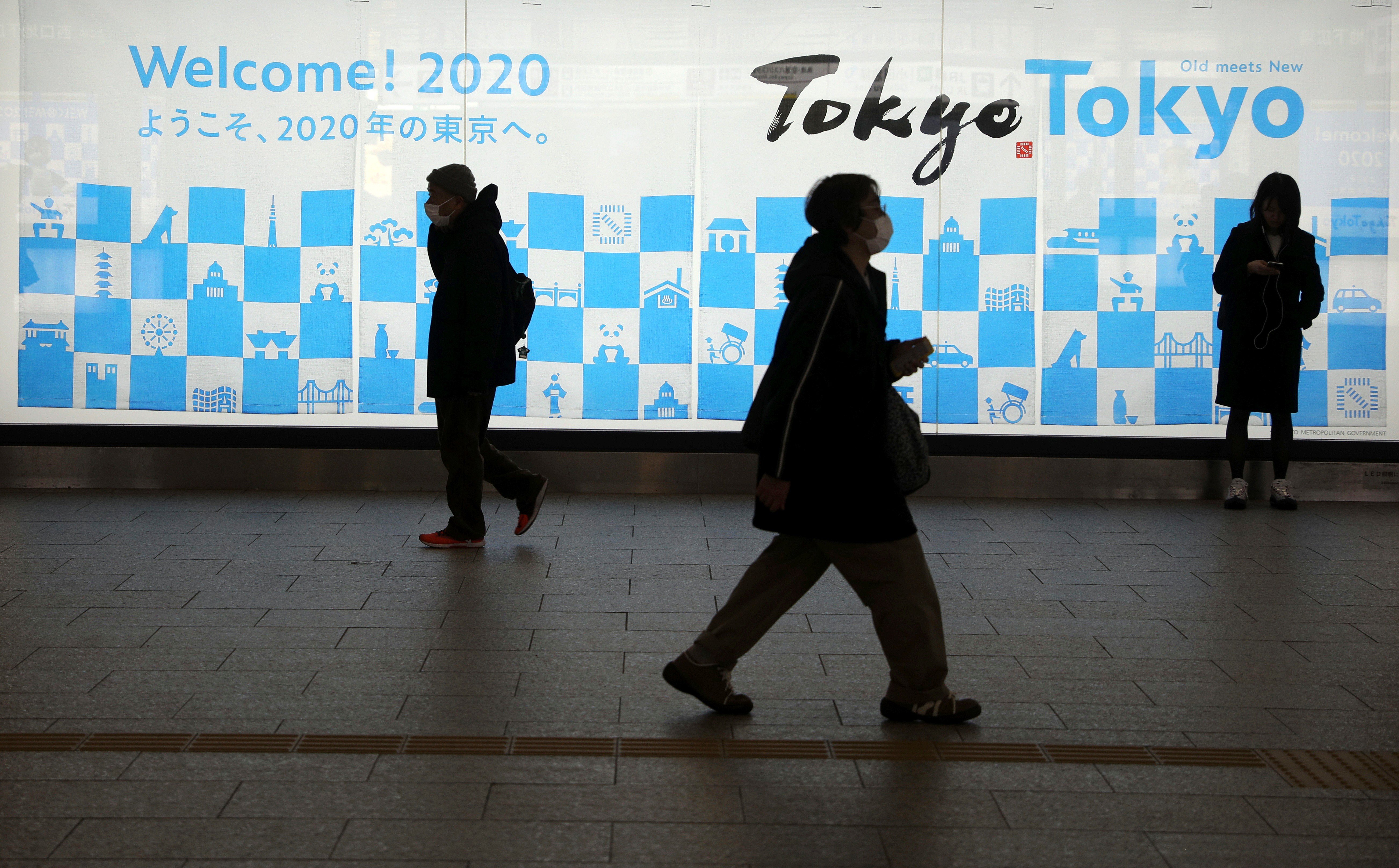 People wearing protective masks walk by a billboard for the Tokyo 2020 Olympics near the Shinjuku station in Tokyo. Photo: Reuters