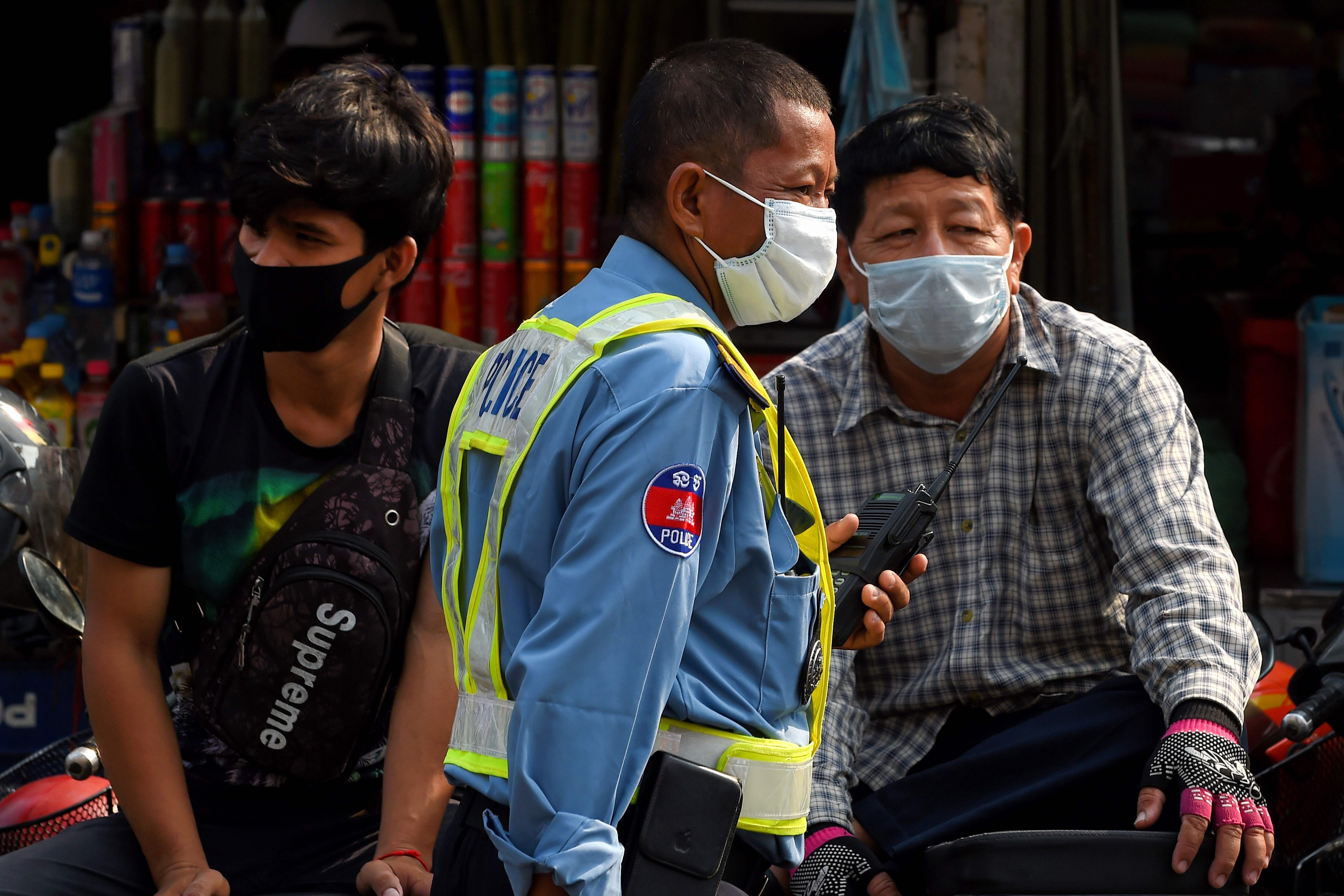 A policeman in Phnom Penh some passers-by wear face masks amid the spread of the novel coronavirus. Photo: AFP