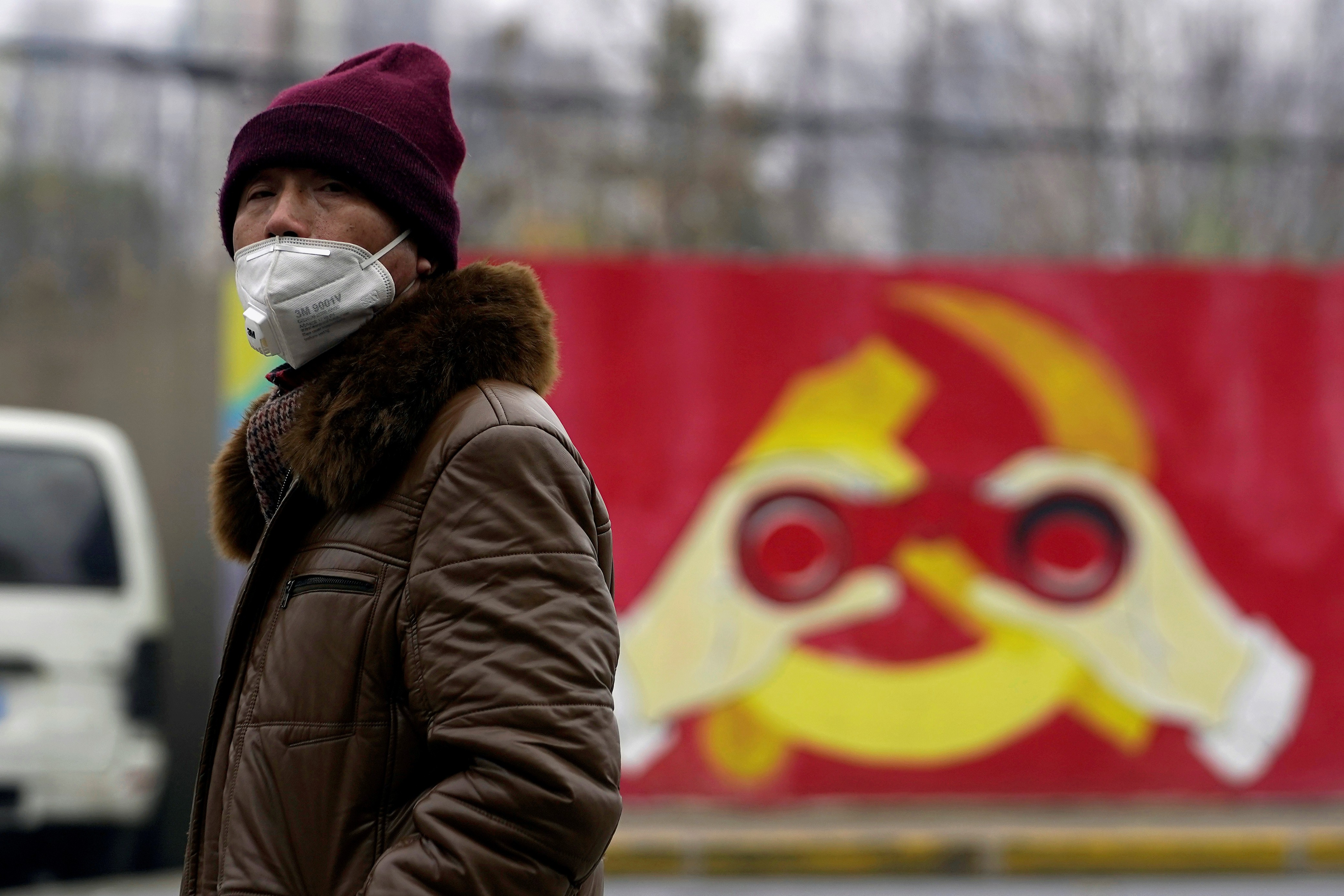 A man wearing a mask walks past a mural showing a modified image of the Communist Party emblem in Shanghai. Photo: Reuters