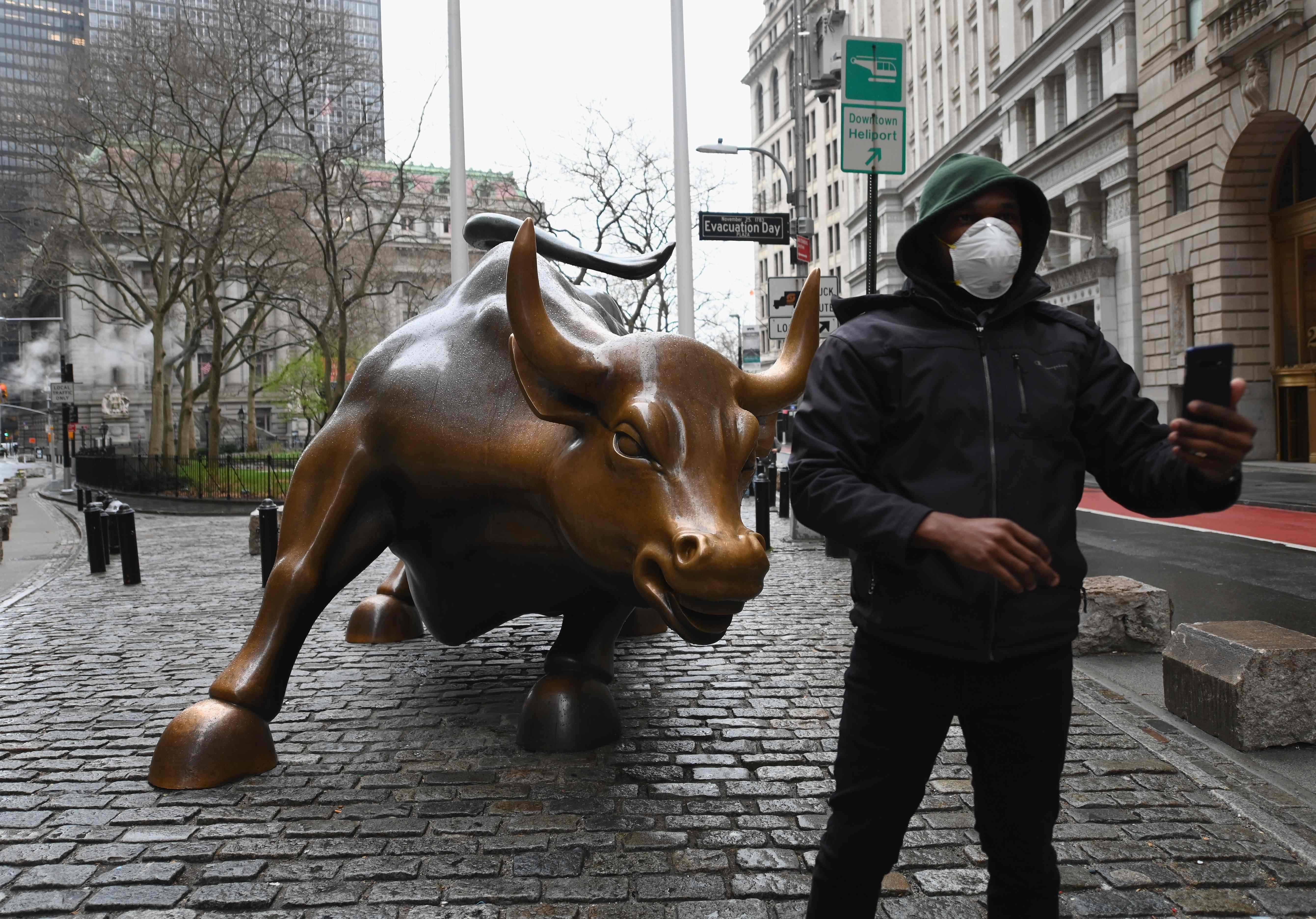A man wearing a face mask takes a picture at the charging bull statue near the New Stock Exchange on Monday. Stocks on Wall Street fell early as Congress wrangled over a massive stimulus package. Photo: AFP