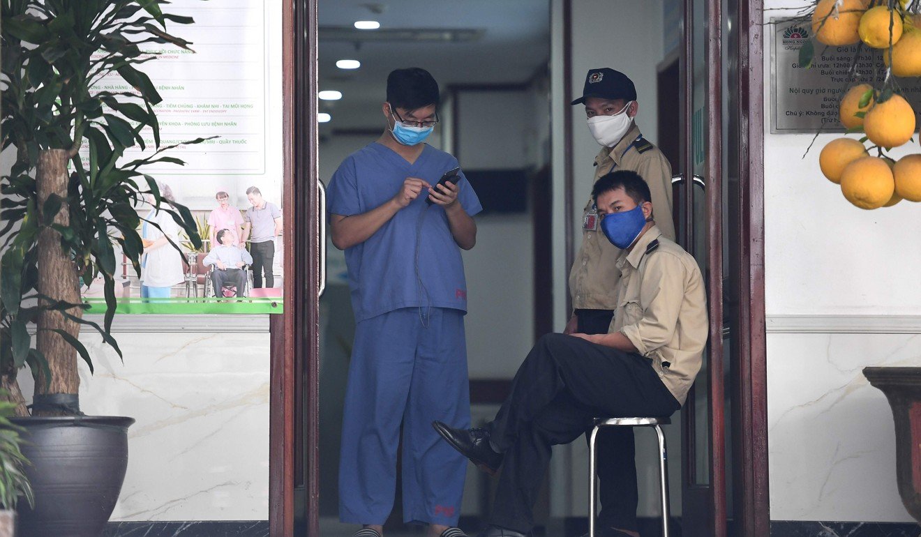 A medical staff member and security guards wearing face masks stand at the entrance of a private hospital under quarantine following a visit by a Vietnamese woman who arrived from London and later tested positive for coronavirus. Photo: AFP