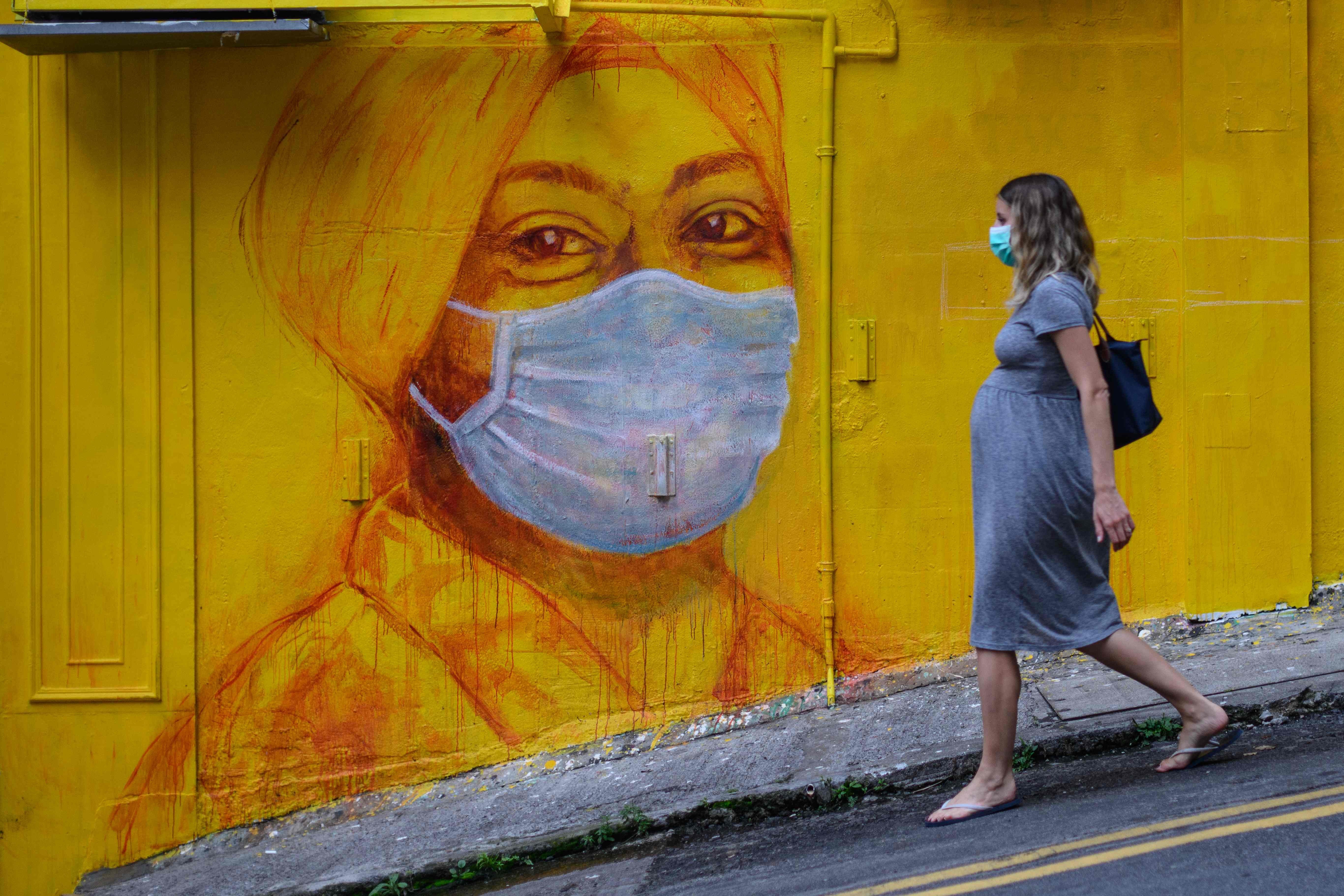 A pregnant woman wearing a mask walks past a street mural in Hong Kong on March 23. Photo: AFP