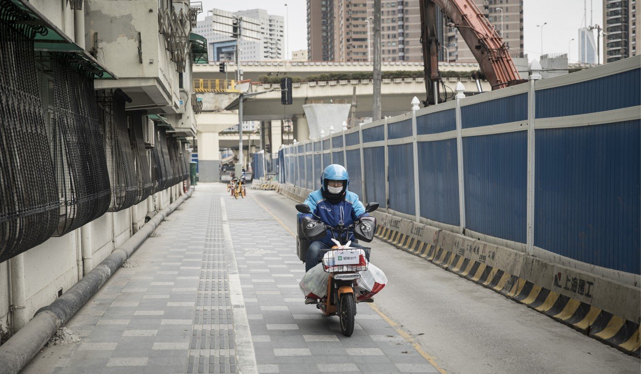 A motorcycle courier wearing a protective face mask makes a grocery delivery on the first day of work after the extended Lunar New Year holiday in Shanghai on February 10. As Chinese-based manufacturers began to restart factories, it is still not clear when they'll be back at full speed. Photo: Bloomberg