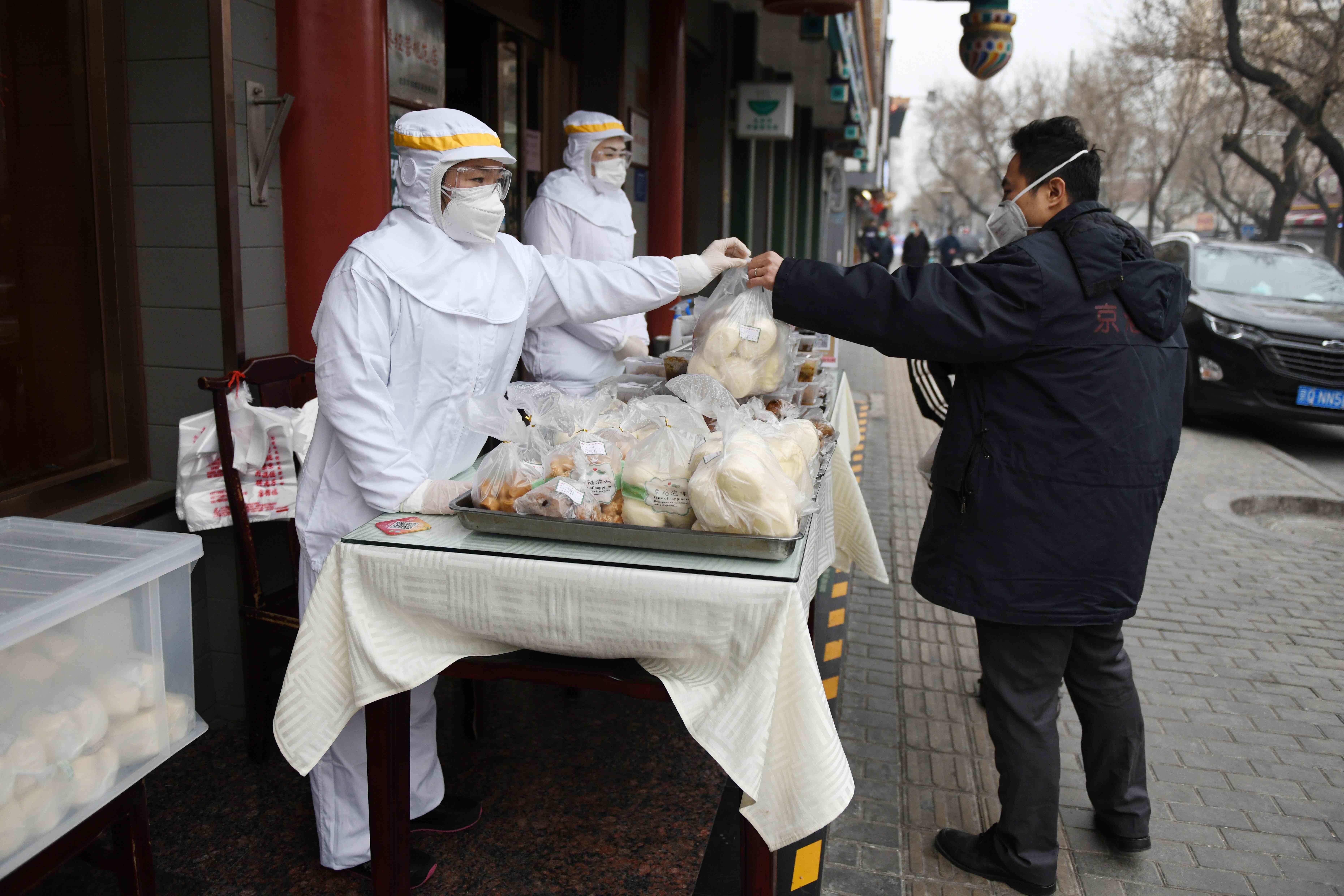 A worker in protective clothing passes a bag of food to a customer on the street outside a restaurant in Beijing. Photo: AFP