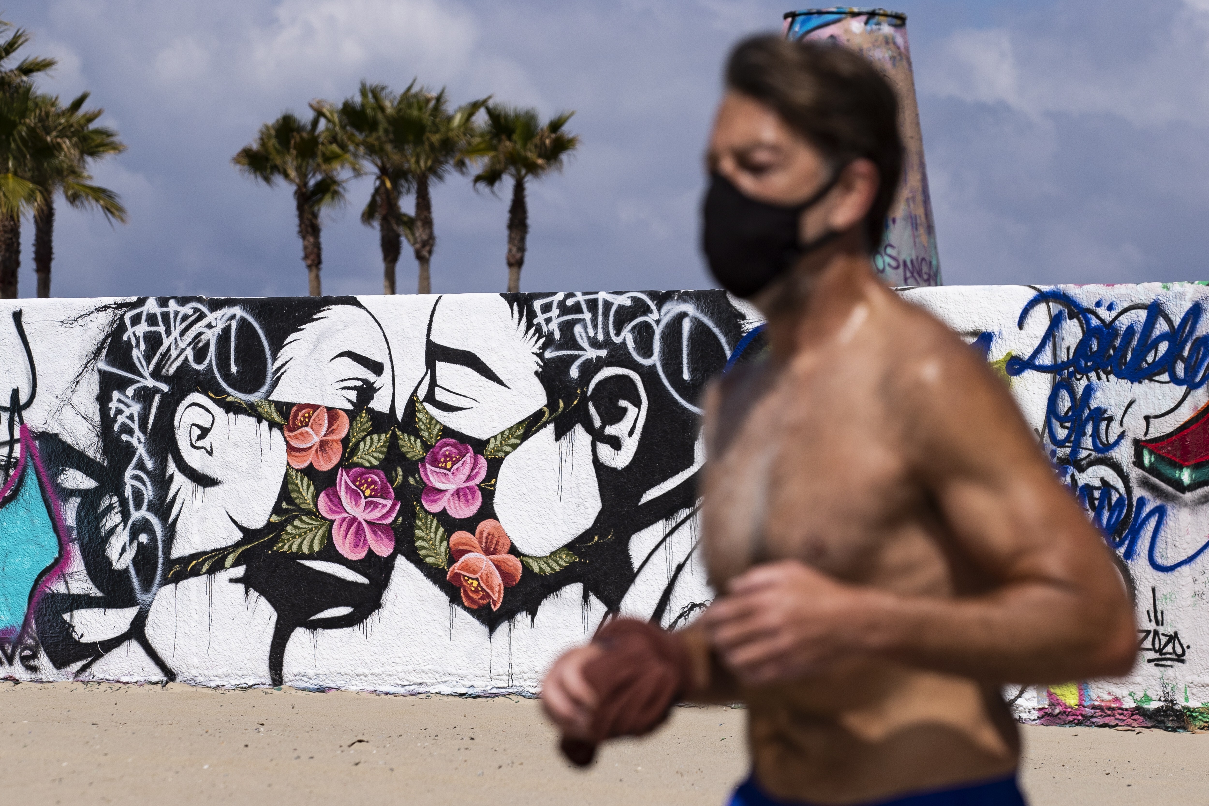 A runner in a face mask jogs past a mural in Venice, California, showing a masked couple kissing. Photo: EPA-EFE