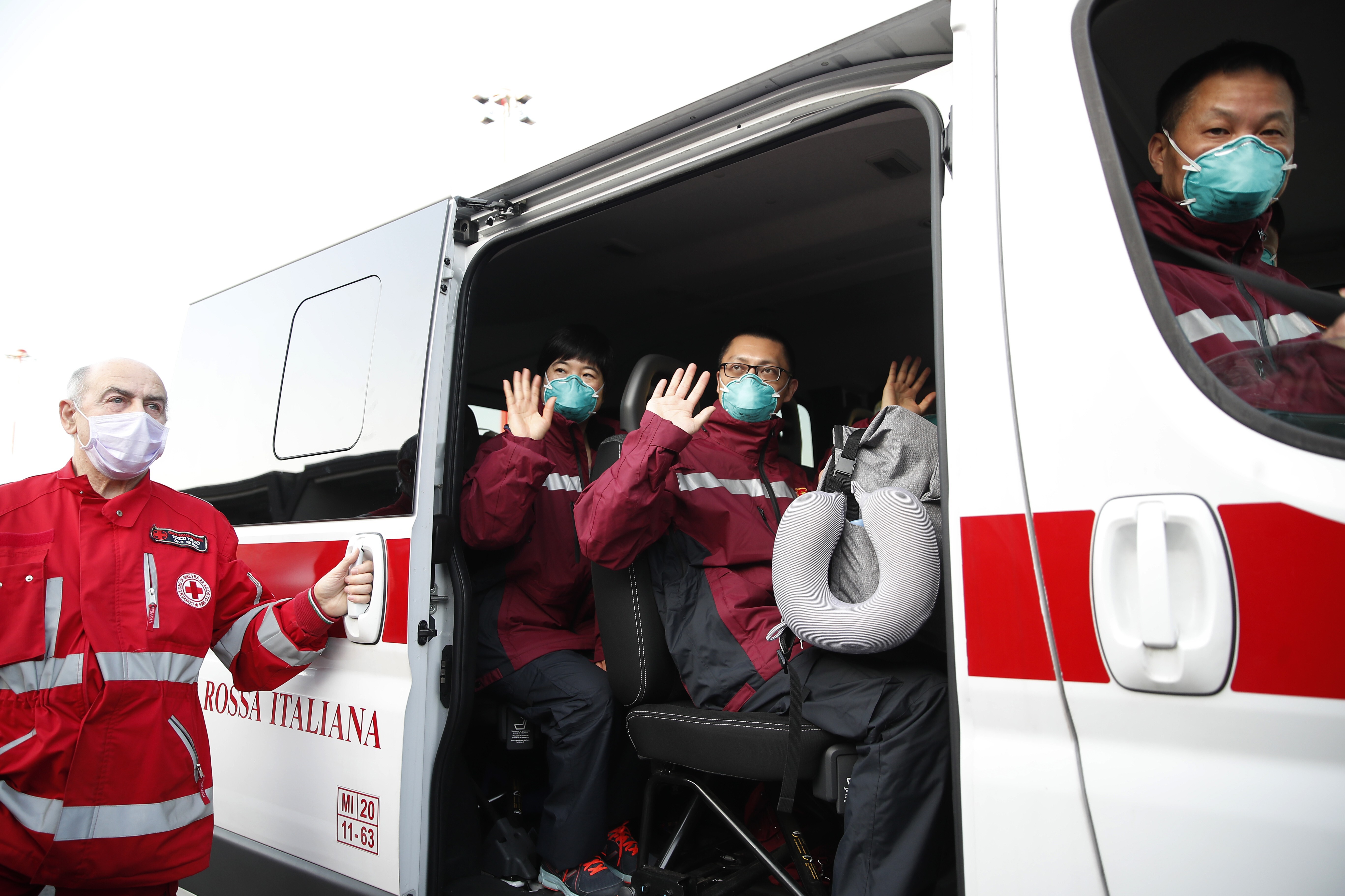 Doctors and paramedics from China wave on a Red Cross vehicle after arriving at Malpensa airport, Milan, on March 18, part of a team of 37 and a shipment of 20,000 tonnes of equipment sent to help Italy. Photo: AP