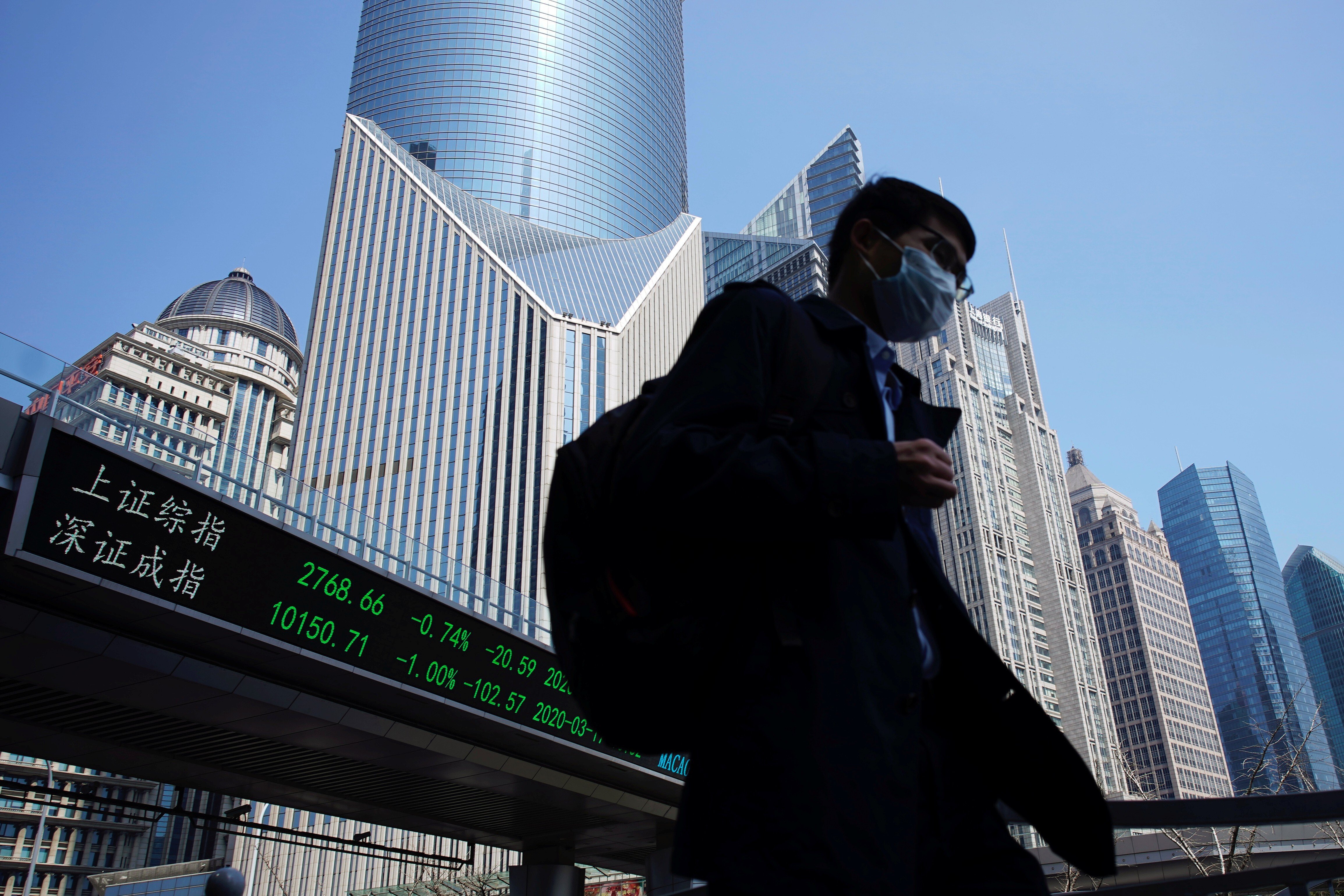 A pedestrian wearing a face mask walks near an overpass with an electronic board showing information on Shanghai stock exchange. Photo: Reuters