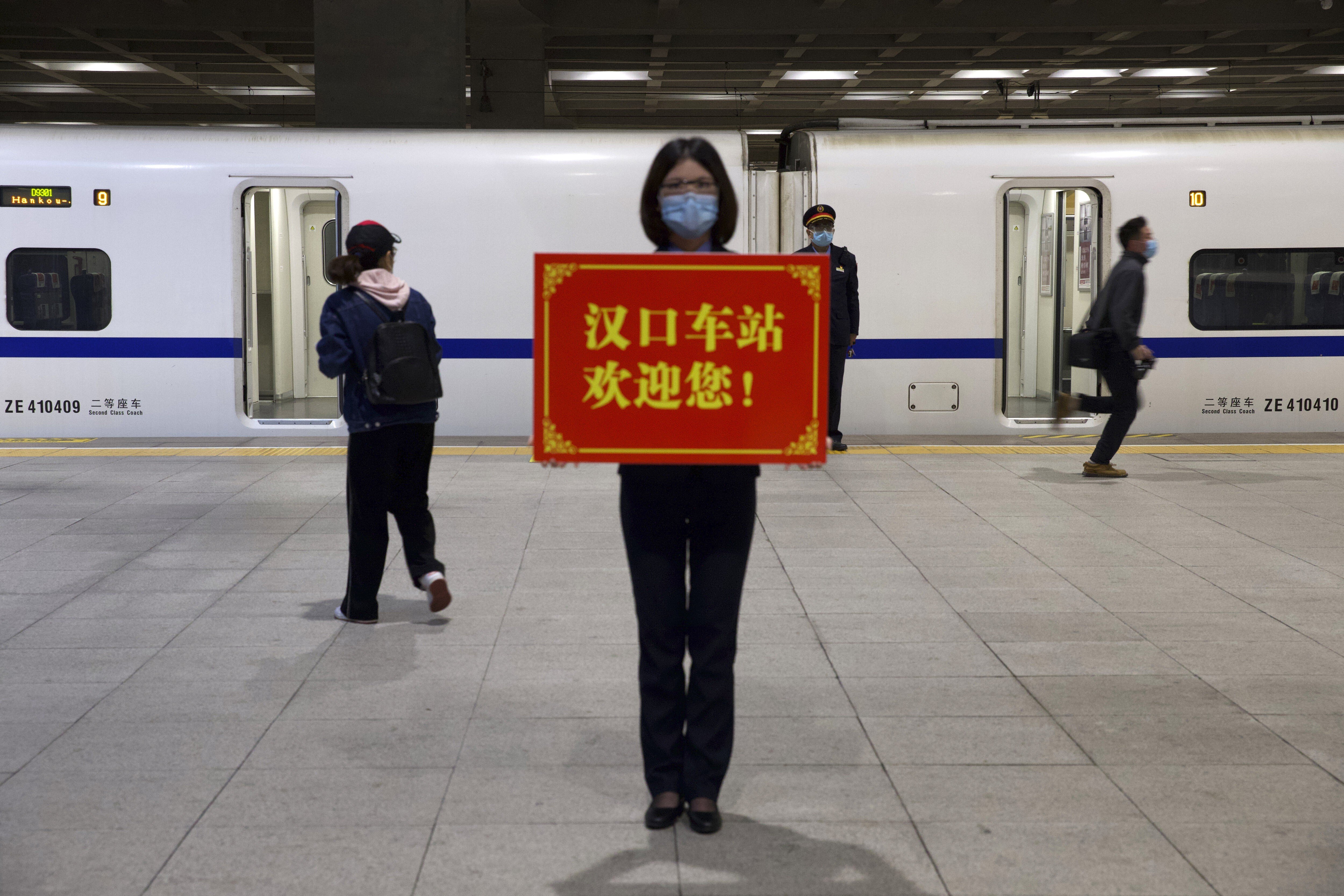 A railway worker holds a sign reading “Hankou Station welcomes you!” as passengers board the first high-speed train to leave after the resumption of services in Wuhan, Hubei, on April 8, after 11 weeks of lockdown. Photo: AP