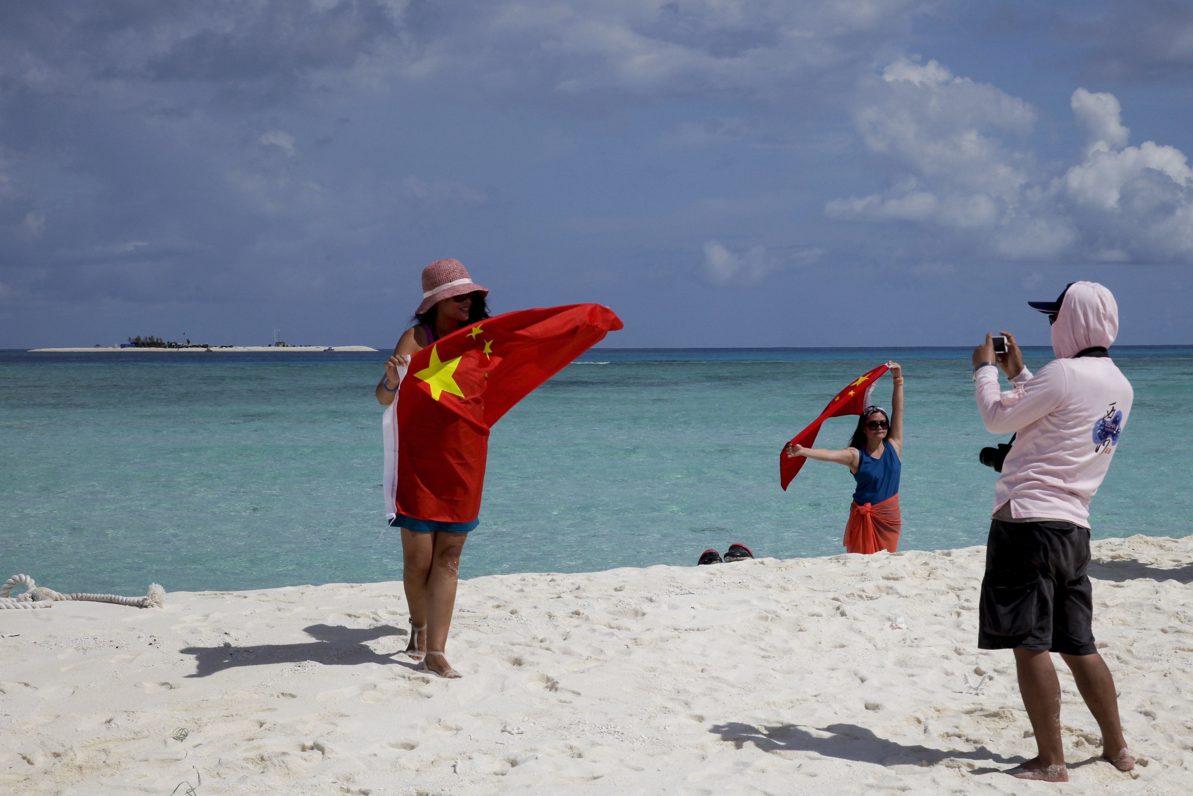 Chinese tourists take souvenir photos with the national flag on Quanfu, one of the Paracel Islands, in Sansha prefecture of Hainan province in the South China Sea, in September 2014. Photo: AP