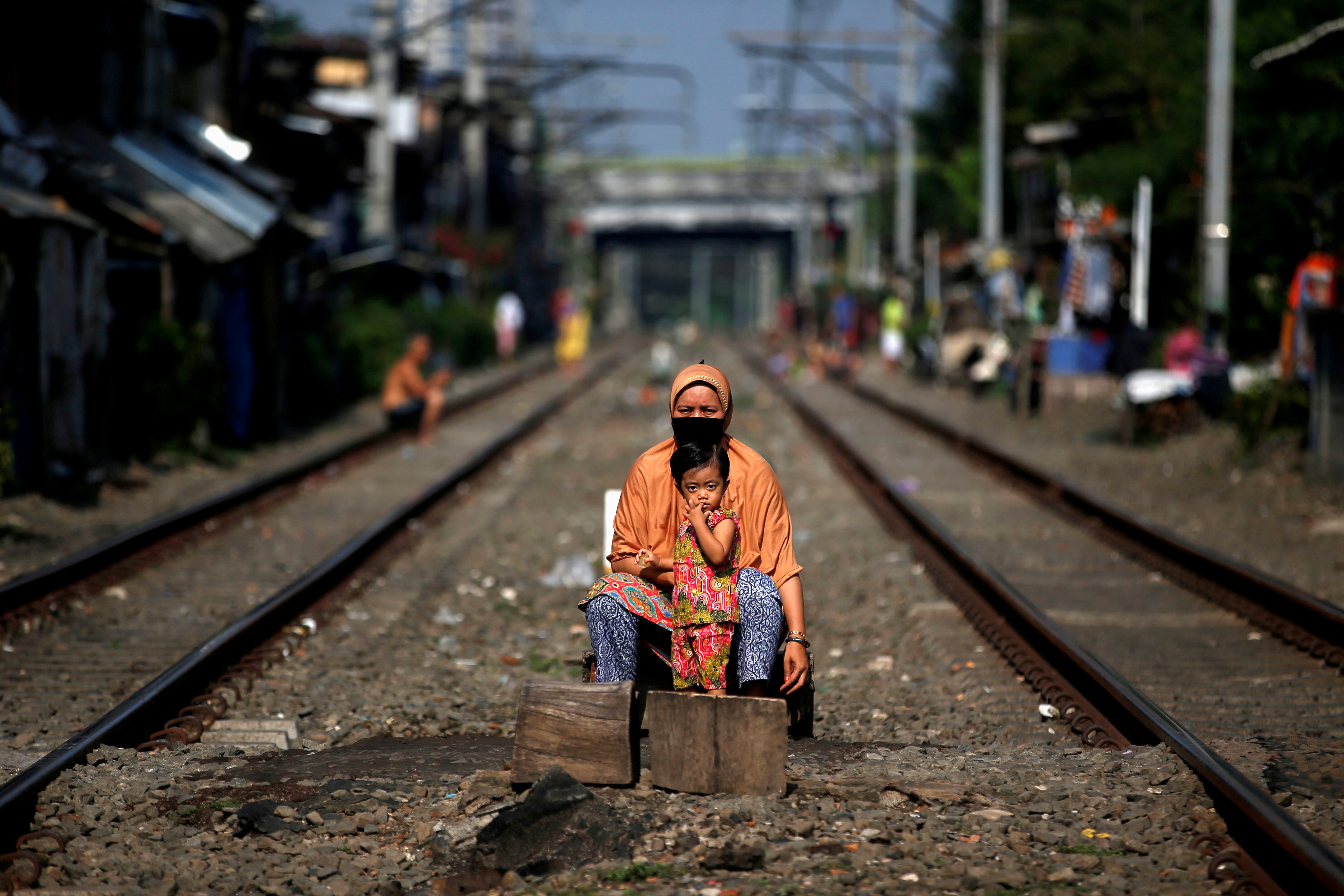 A woman wearing a face mask sits with a child between railway tracks in Jakarta, Indonesia, on April 12, during the imposition of large-scale social restrictions by the government to prevent the spread of Covid-19. Photo: Reuters