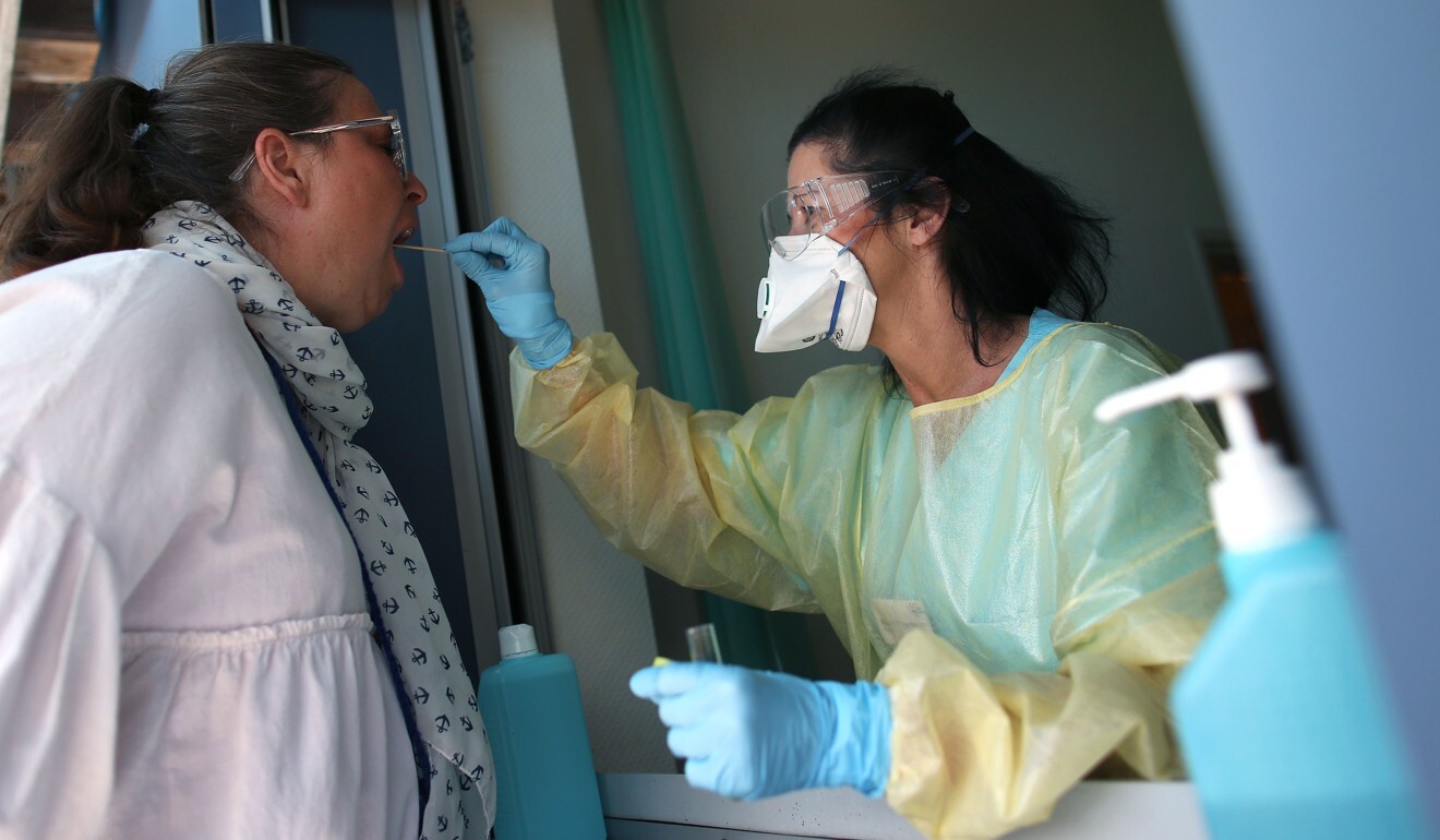 A hospital worker takes a sample from a nurse at a testing point for medical staff in Germany on April 16, 2020. Photo: AFP