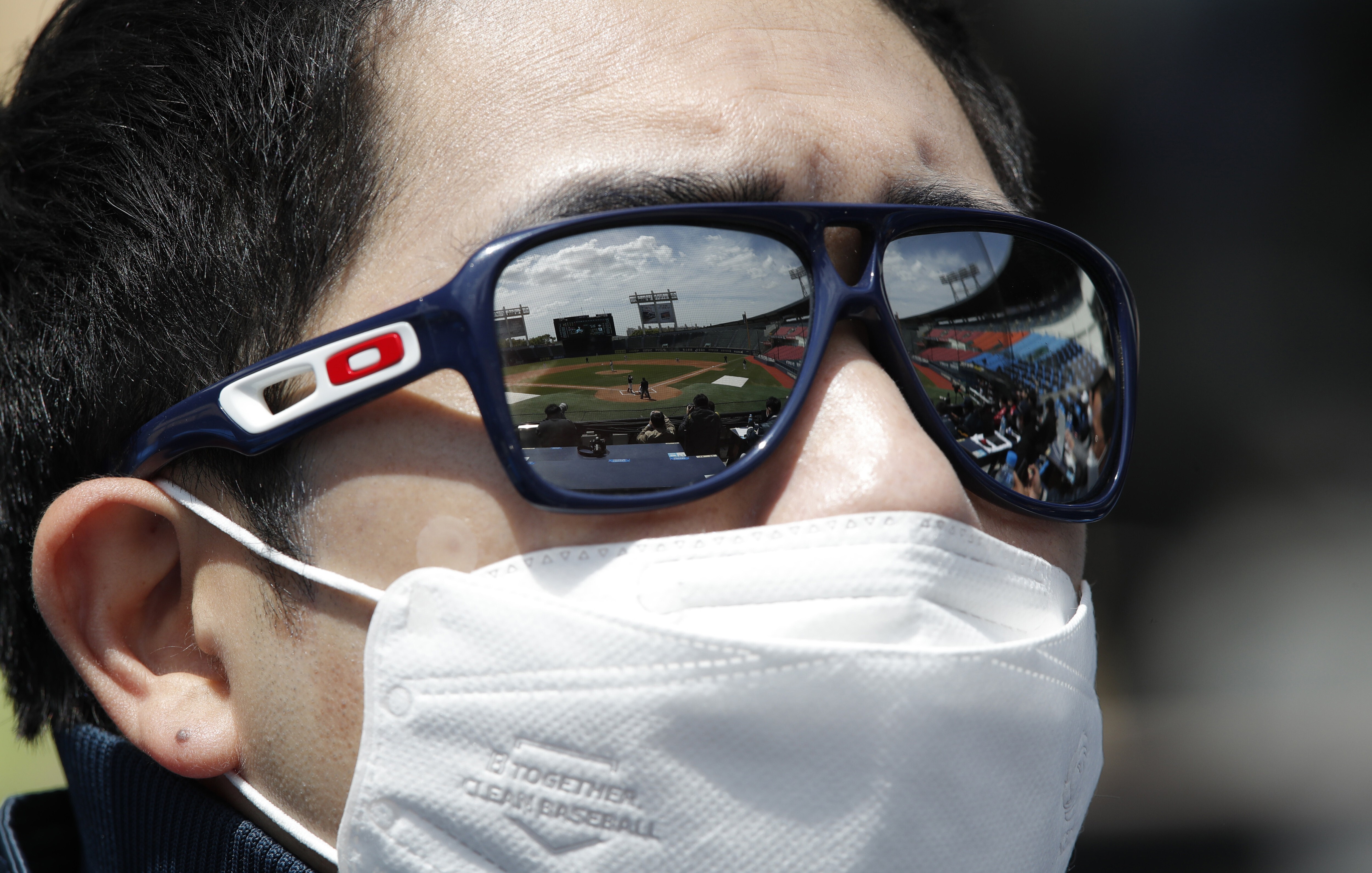 Empty spectator seats are reflected on the sunglasses of a team member wearing a mask as a precaution against the new coronavirus during the pre-season baseball game between Doosan Bears and LG Twins in Seoul, South Korea, Tuesday, April 21, 2020. South Korea's professional baseball league has decided to begin its new season on May 5, initially without fans, following a postponement over the coronavirus. (AP Photo/Lee Jin-man)