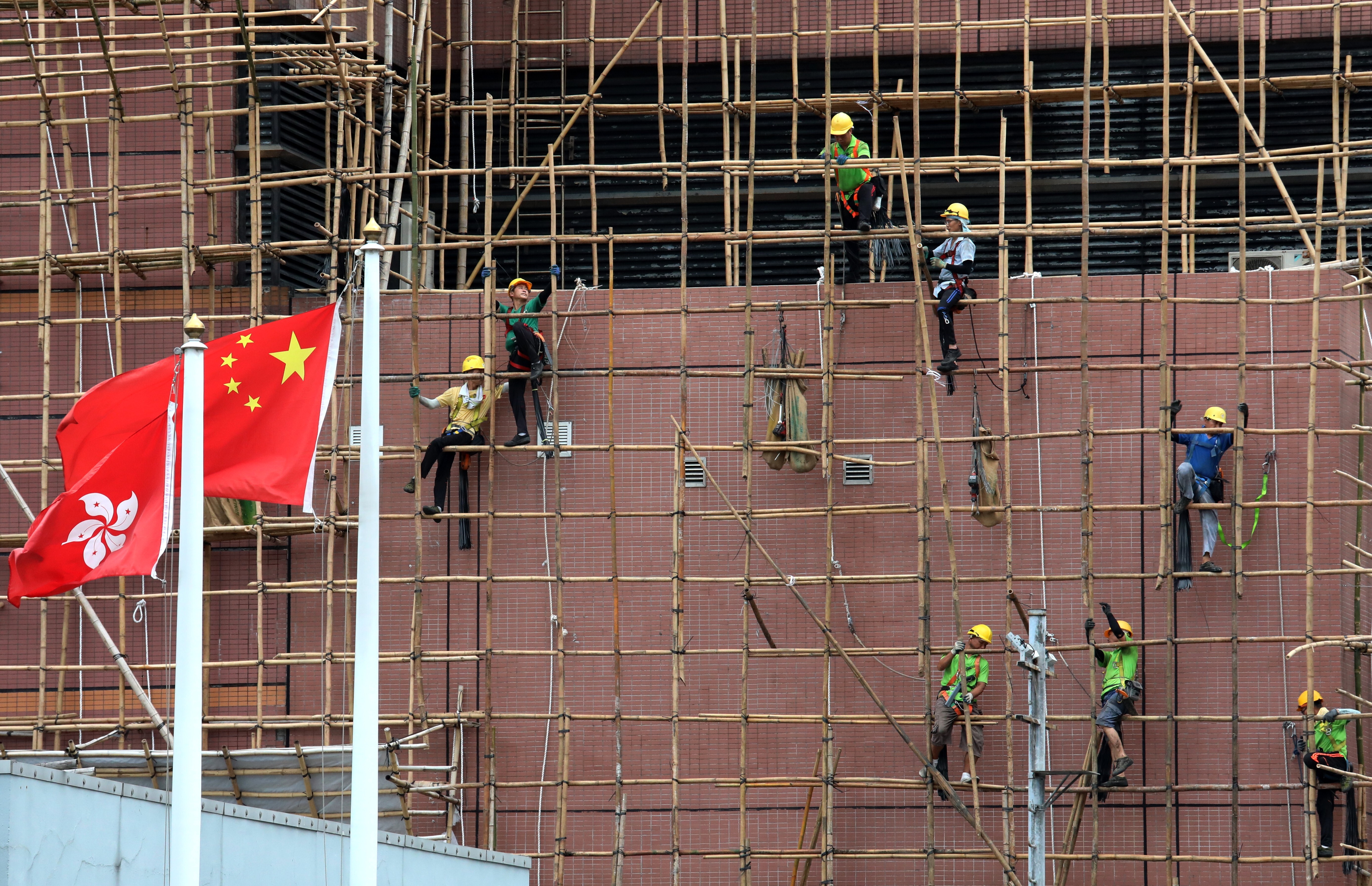 Construction workers remove the scaffolding on a building in Sham Shui Po as the Hong Kong and Chinese flags flutter in the foreground, in June 2019. Photo: Felix Wong