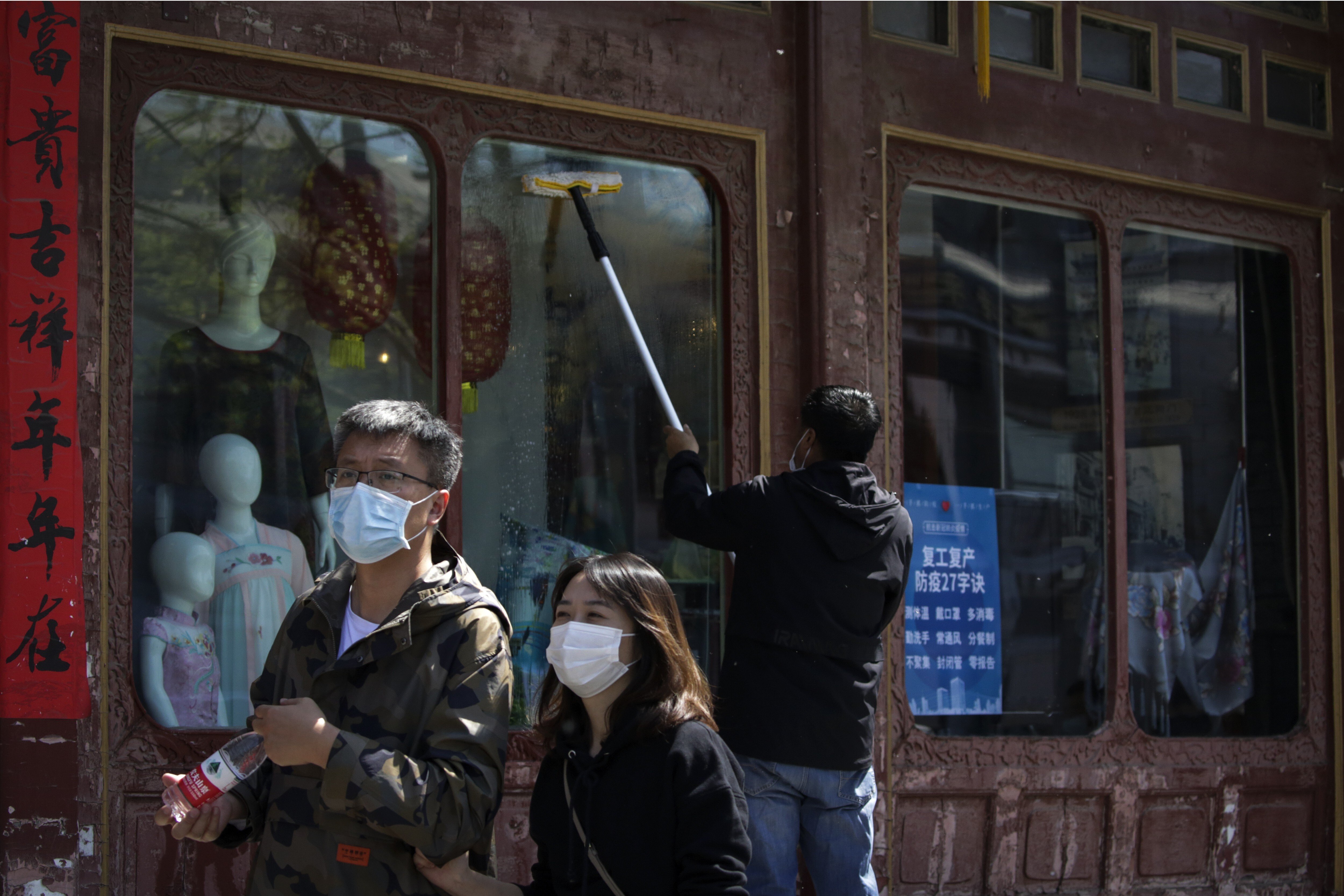 People walk past a worker wiping the window of a clothing shop in Beijing displaying a notice about work resumption and pandemic prevention. Photo: AP