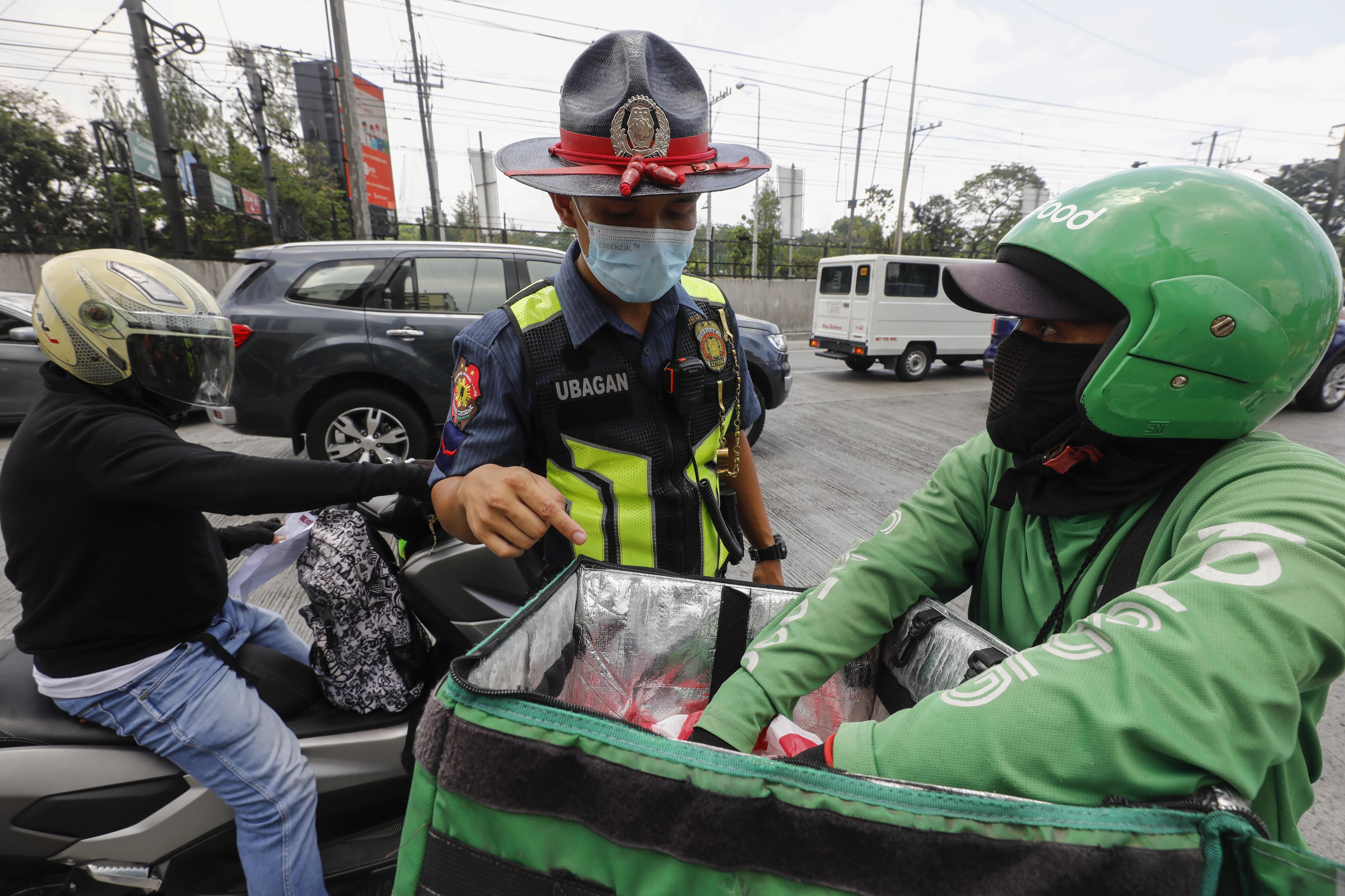 A police officer checks what a food delivery worker was transporting in Metro Manila earlier this month amid the coronavirus quarantine. Photo: EPA