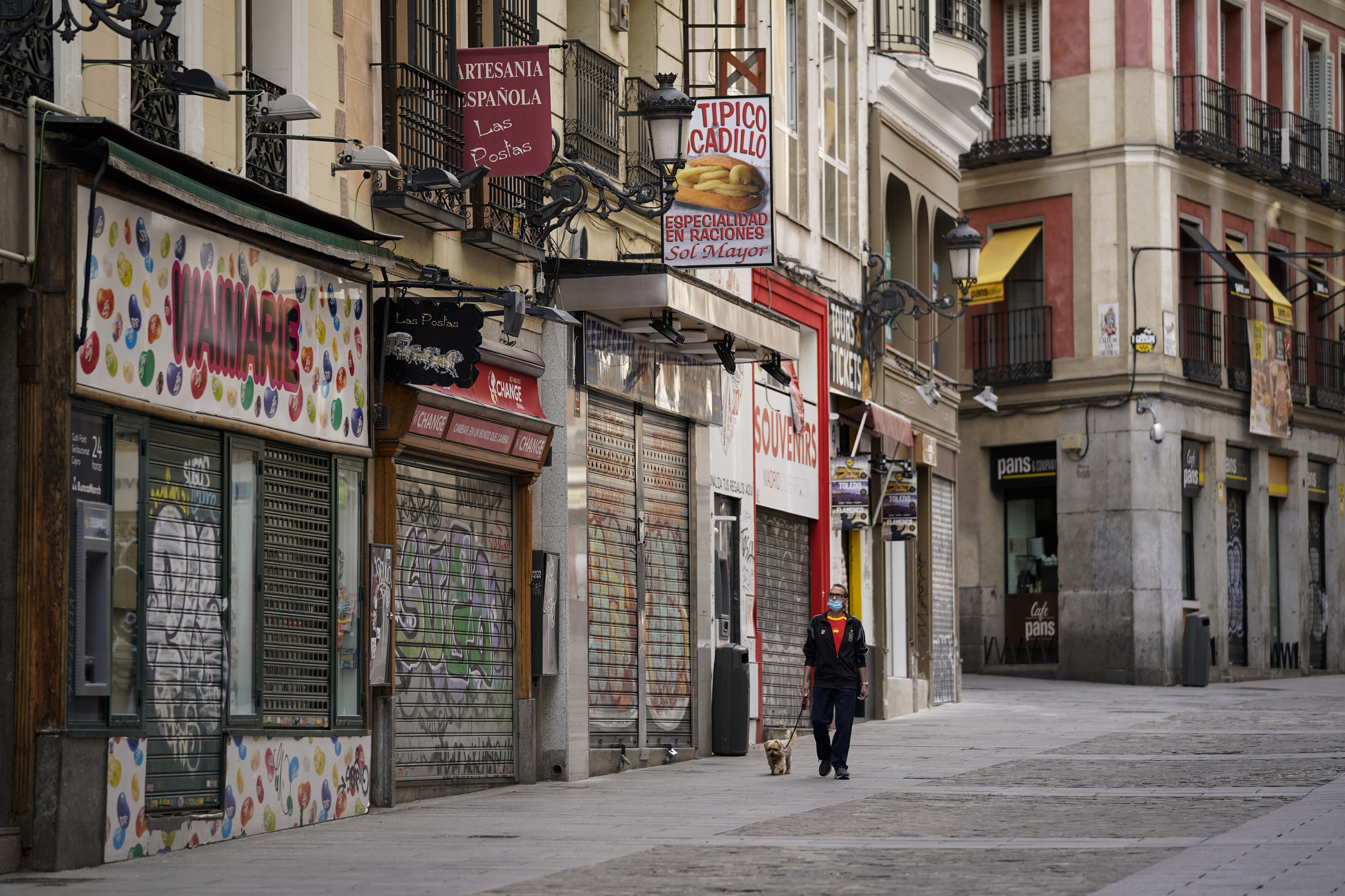 A pedestrian walks a dog along a street lined with closed cafes and shops in Madrid on May 7. Photo: Bloomberg