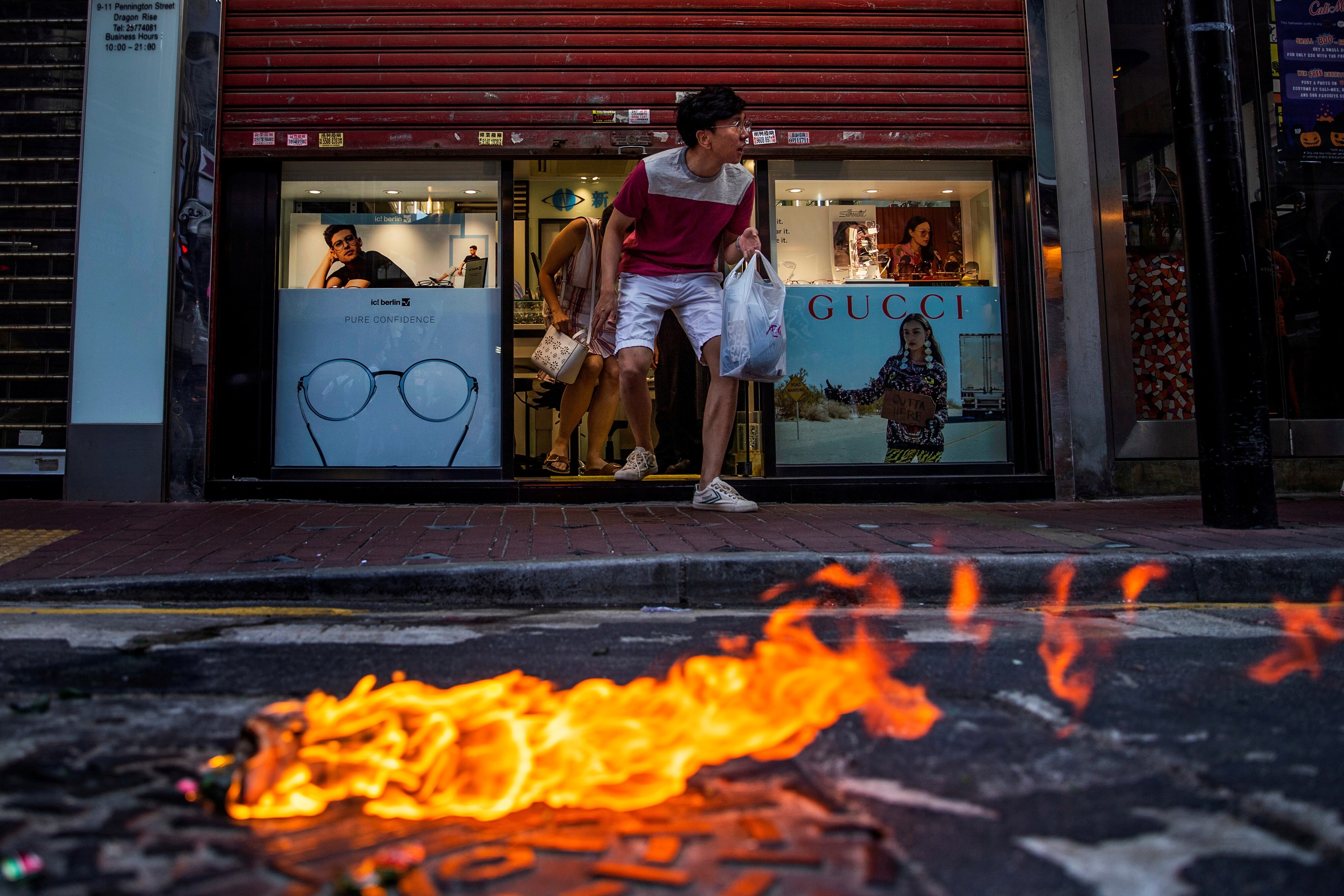 Customers cautiously exit a store in Hong Kong, as a Molotov cocktail burns on the street during a clash between protesters and riot police on November 2, 2019. Photo: Reuters