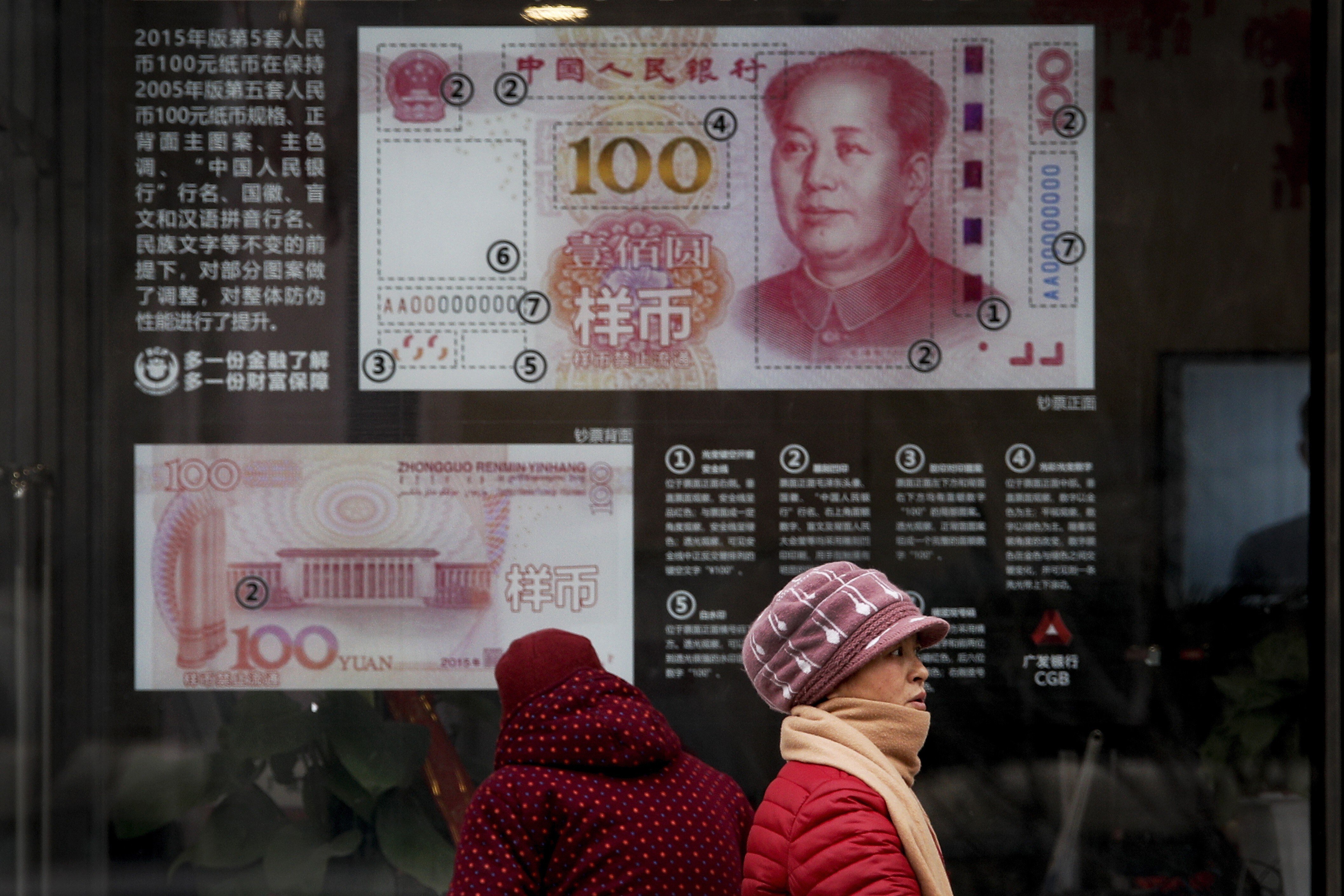A woman walks past a bank window panel displaying the security markers on the latest 100 yuan notes in Beijing on February 18, 2019. Photo: AP