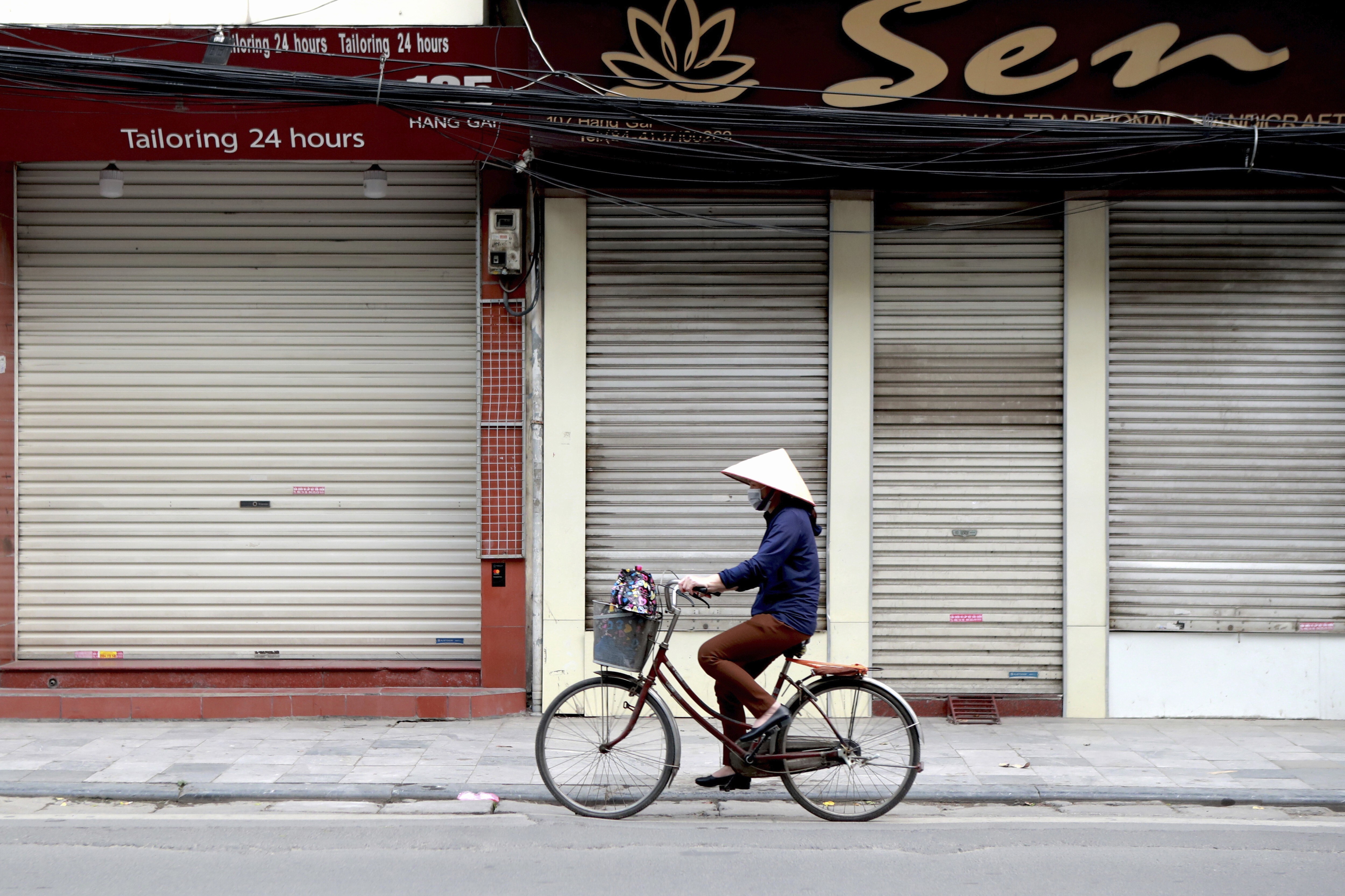 A woman cycles past closed shops in Hanoi, Vietnam, on March 27 after Prime Minister Nguyen Xuan Phuc ordered non-essential business to shut down to curb the spread of Covid-19. Photo: AP