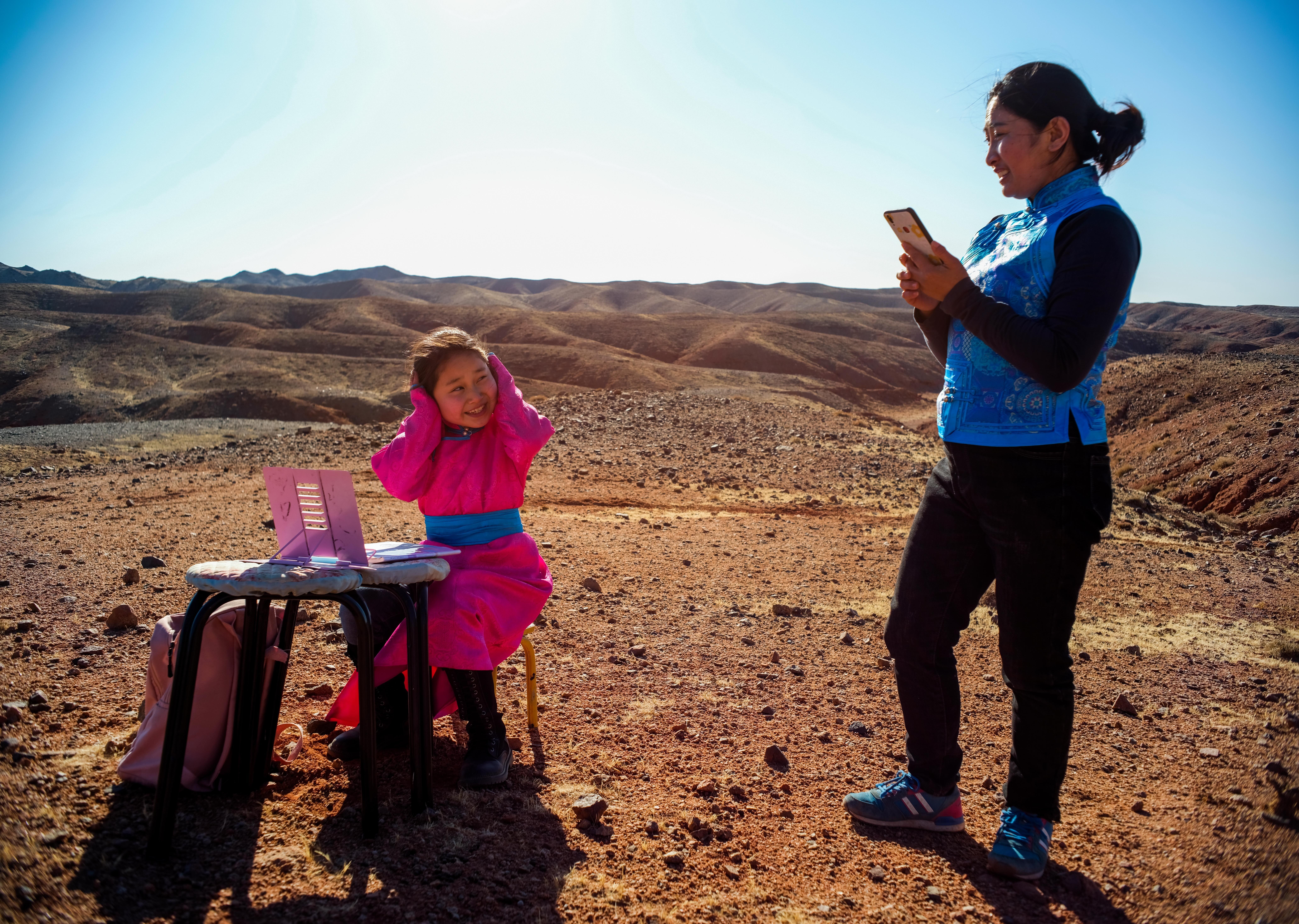 Ce Geng (left) prepares to take an online class as her mother looks on in Alxa Left Banner, in north China’s Inner Mongolia Autonomous Region, on April 1. The nine-year-old’s parents drive her around their ranch to look for better Wi-fi when the weather is bad so she can attend classes online after schools shut due to Covid-19. Photo: Xinhua