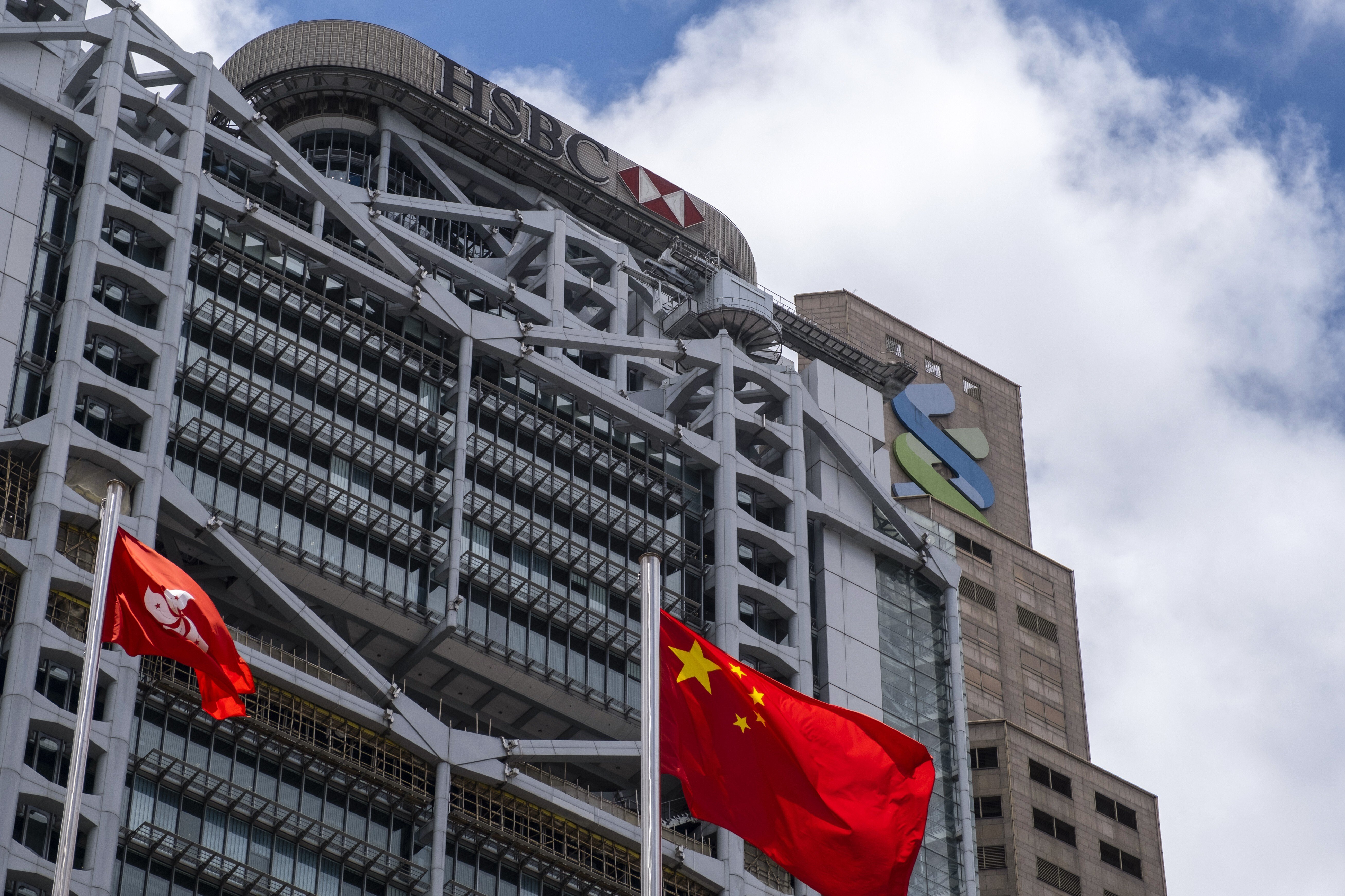 The Chinese and Hong Kong flags fly near the HSBC (left) and Standard Chartered buildings. Participating banks in Hong Kong will start accepting registrations for the government’s HK$10,000 cash payout scheme on June 21. Photo: Bloomberg