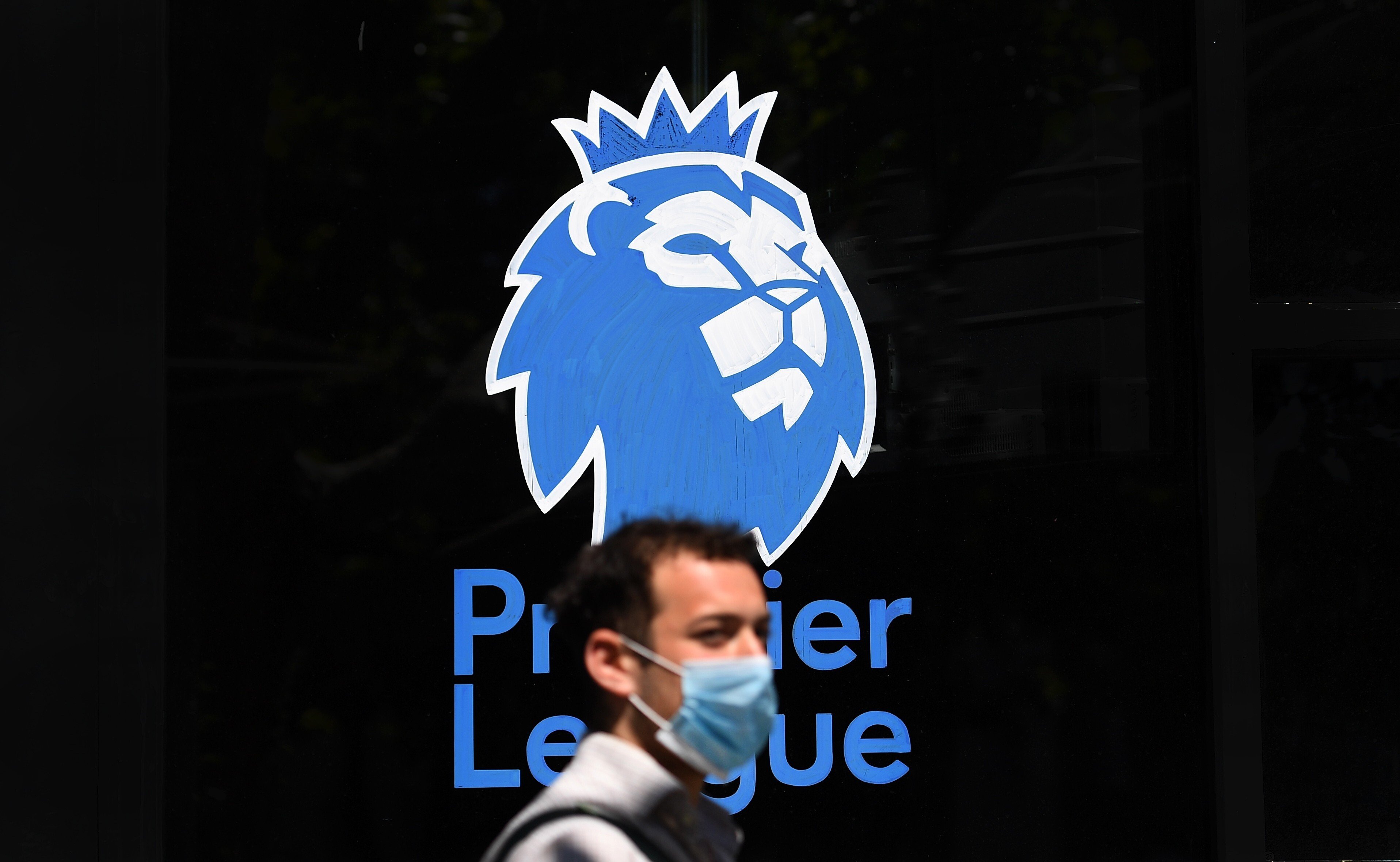 A man wearing a protective mask walks past the English Premier League logo in London. Photo: EPA
