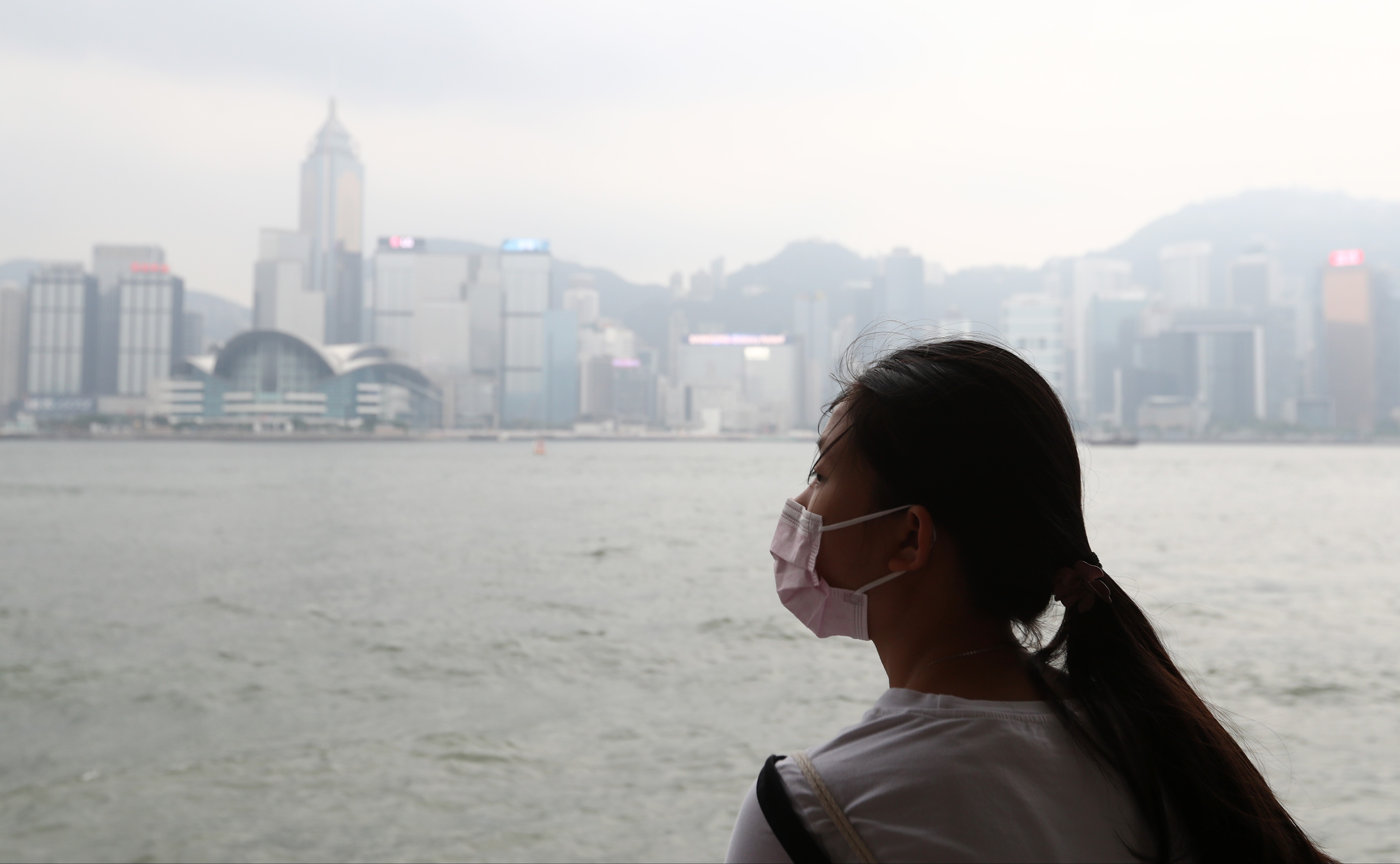 A woman wearing a face mask looks across Victoria Harbour as the Hong Kong skyline is obscured by smog on August 26, 2018. Photo: Nora Tam