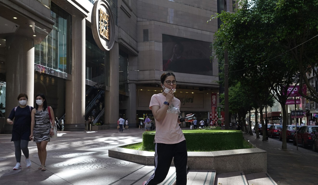 A woman pulls down her face mask to smoke outside a downtown shopping centre in Hong Kong. Photo: AP