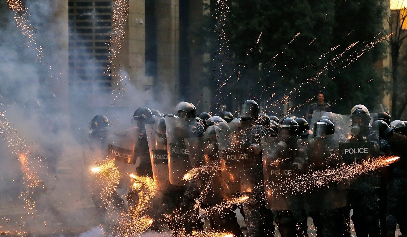 Firecrackers thrown by protesters explode in front of riot police amid clashes in the vicinity of the parliament in central Beirut on August 10. Photo: AFP
