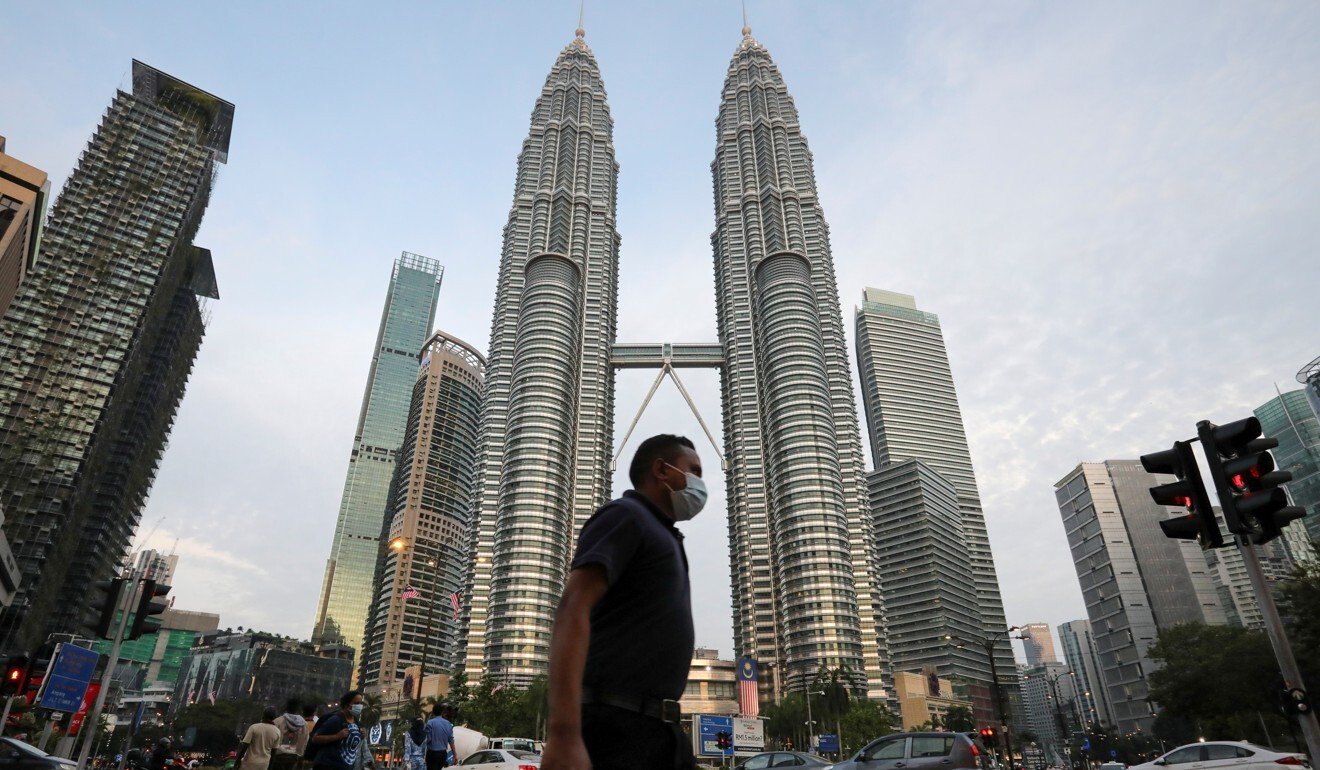 A man wearing a protective mask crosses a street in front of the Petronas Twin Towers, in Kuala Lumpur. Photo: Reuters