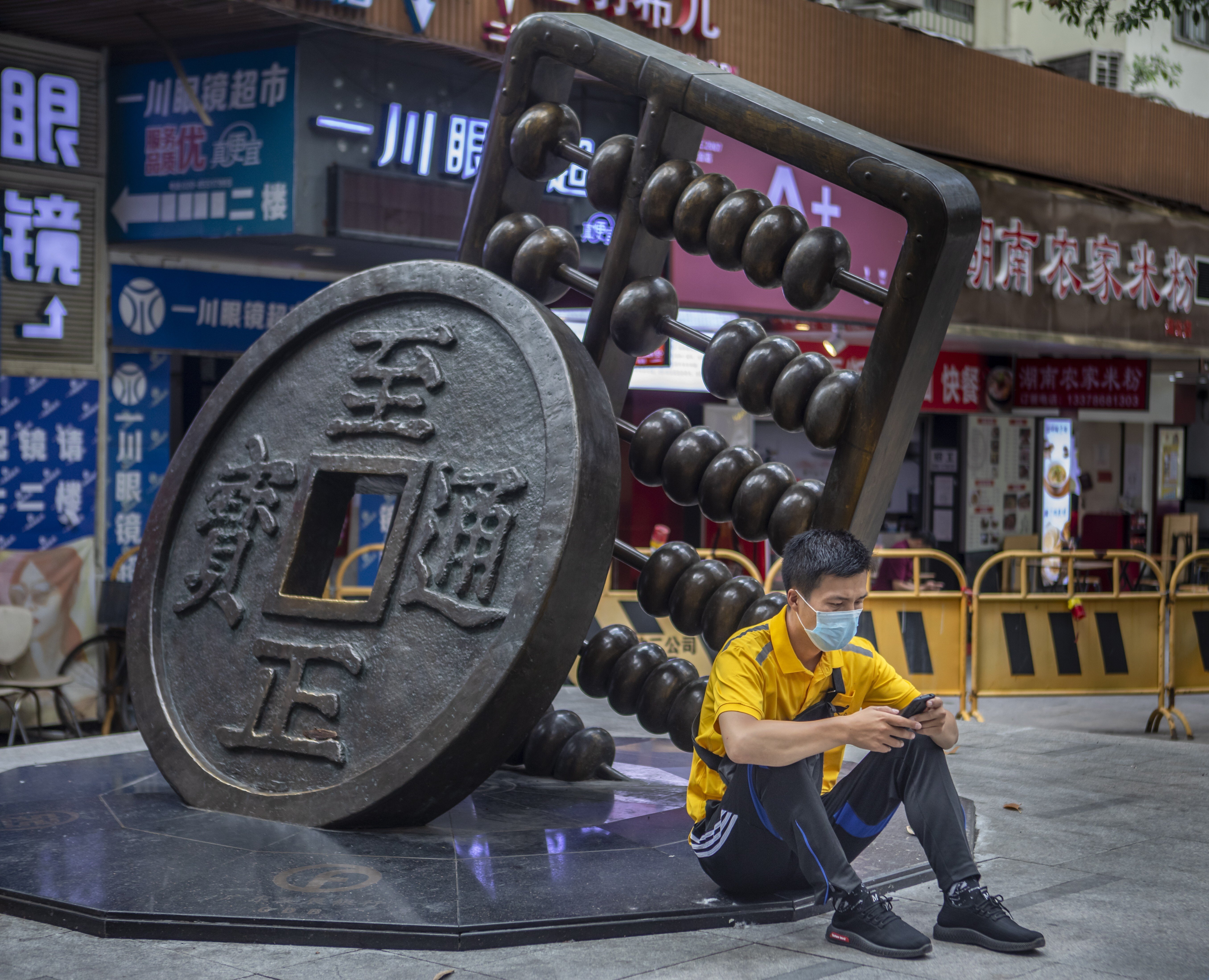 A man uses his cellphone as he sits next to a sculpture representing the renminbi and an abacus in Guangzhou, China, on May 14. China has launched a trial of a new state-run digital currency in four cities: Shenzhen, Suzhou, Chengdu and Xiongan. Photo: EPA-EFE