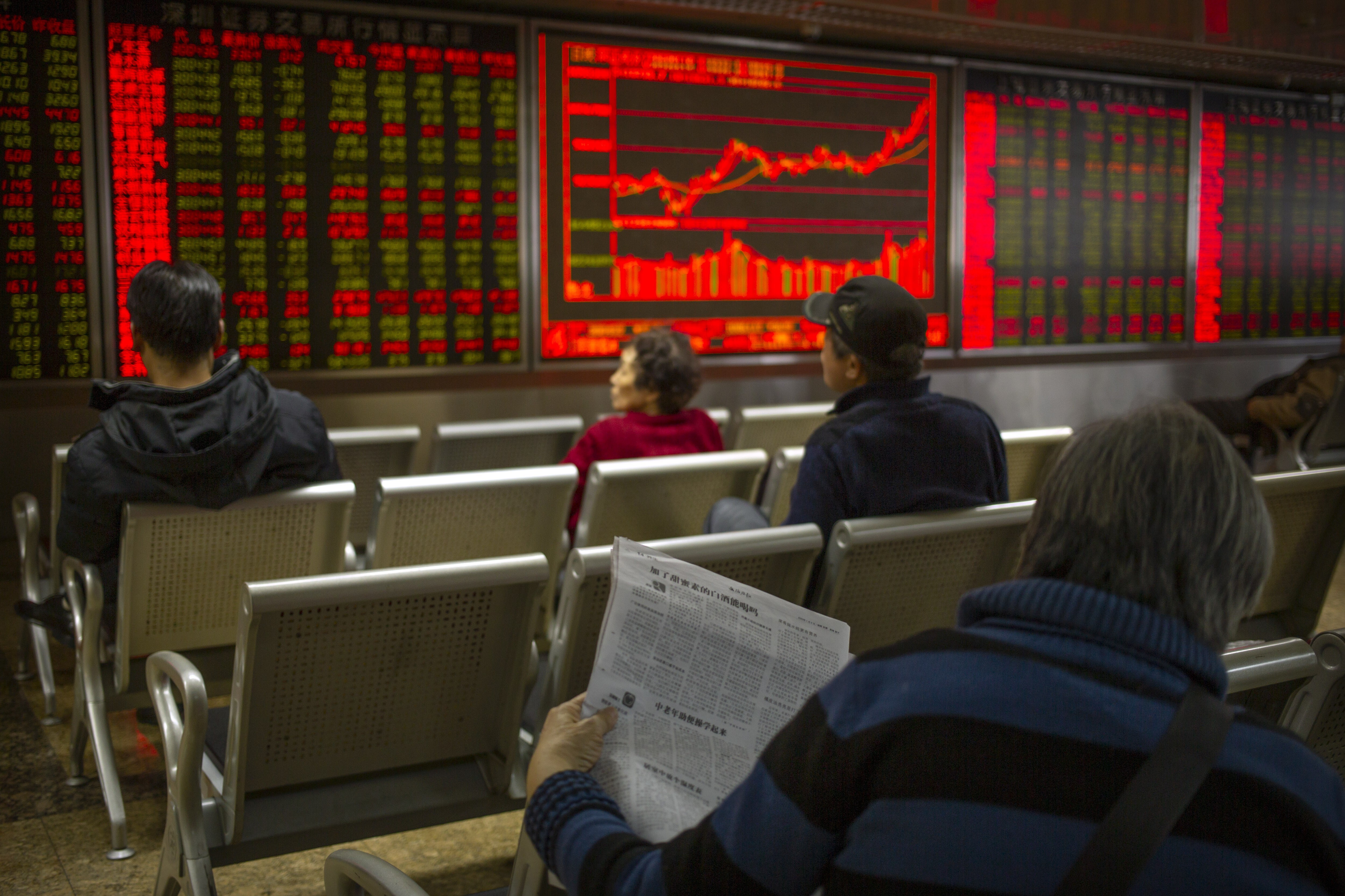 A Chinese investor reads a newspaper as she monitors stock prices at a brokerage house in Beijing. Photo: AP