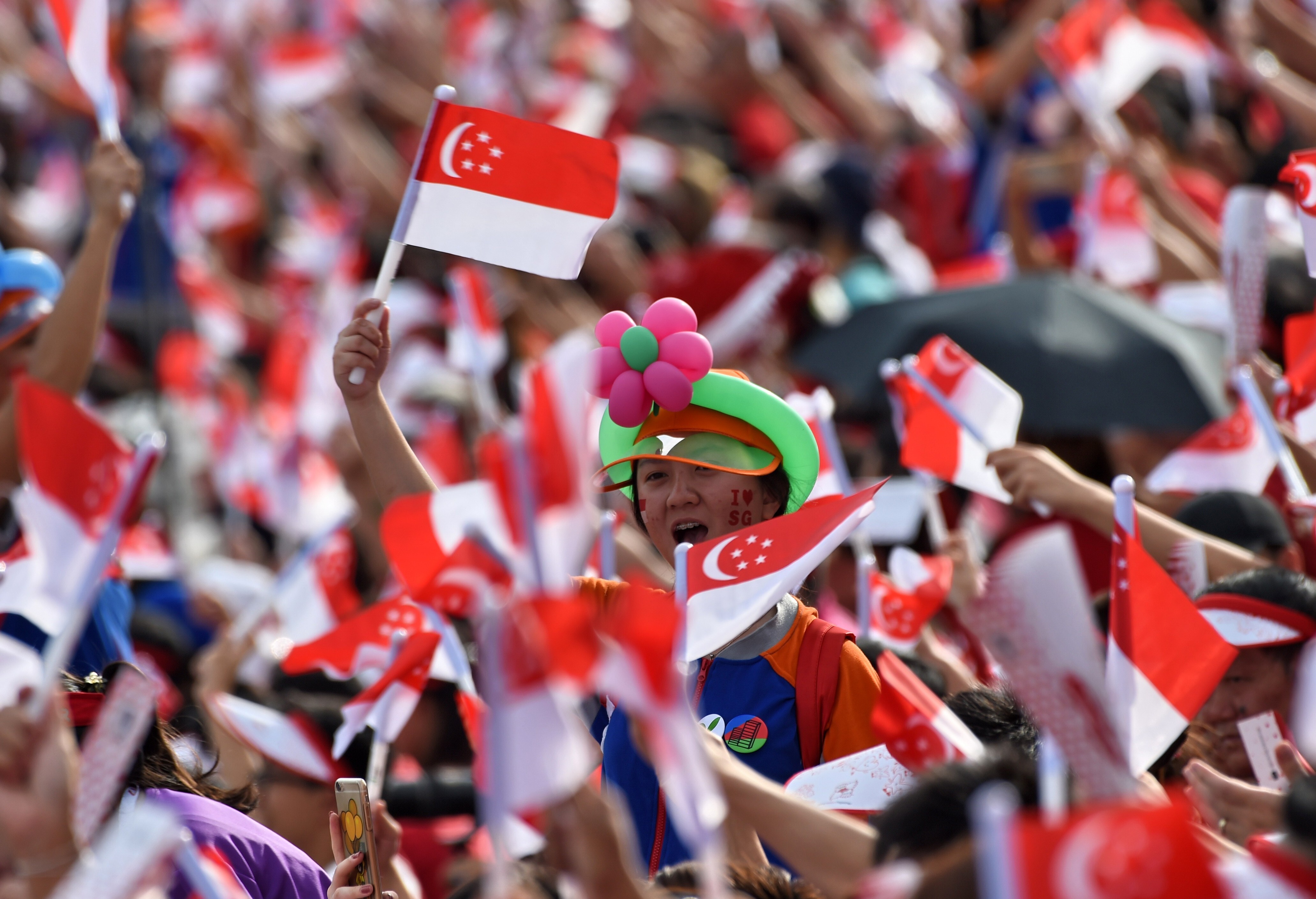 A young Singaporean joins the crowds in waving the country’s flag during National Day celebrations on August 9, 2017. Photo: AFP