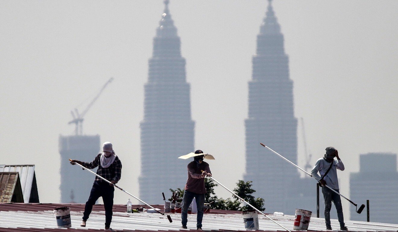 Construction workers paint a factory roof against a background of the Twin Towers of Kuala Lumpur. Photo: EPA