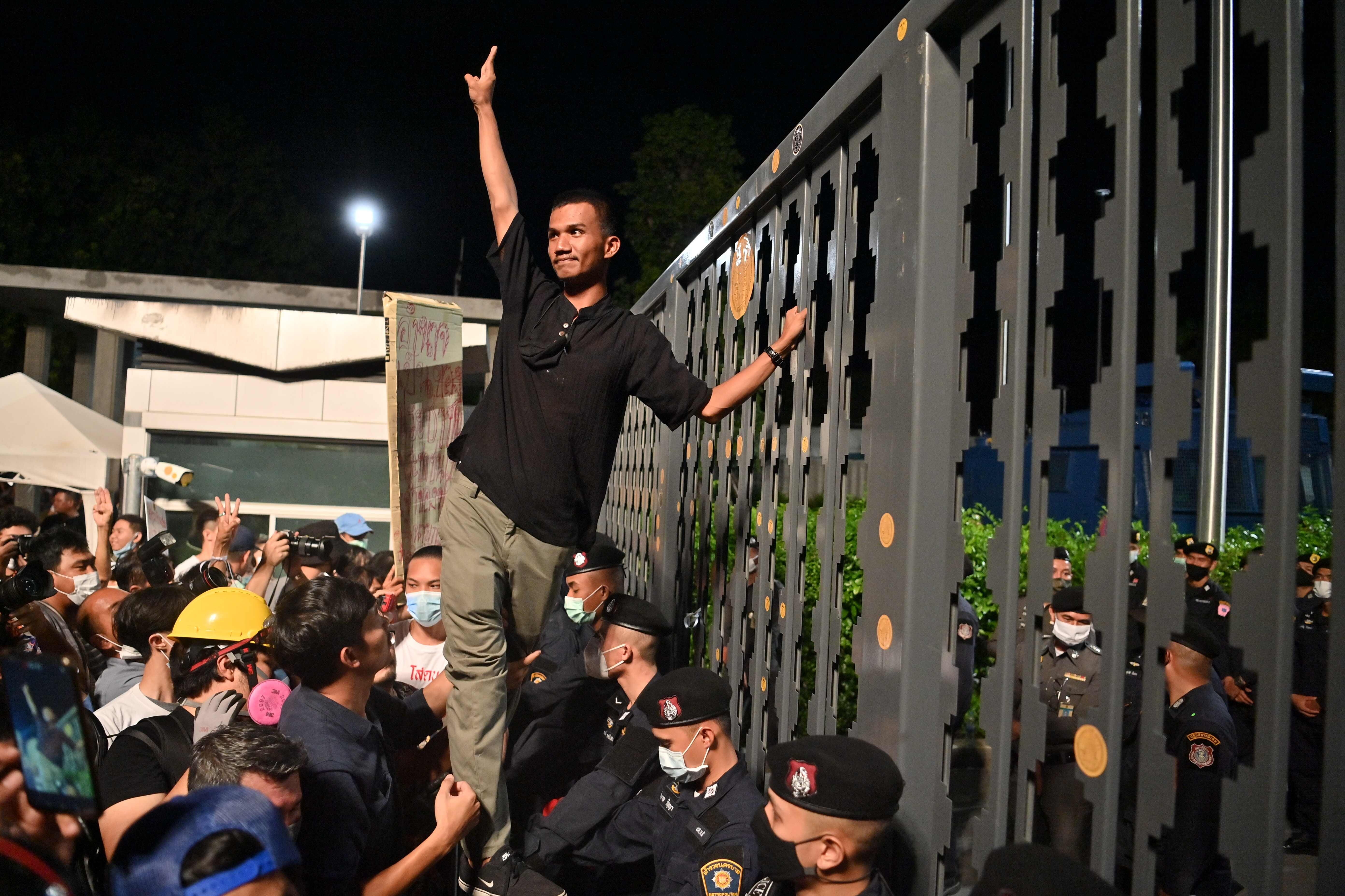 Pro-democracy activist Panupong “Mike” Jadnok makes a three-finger salute to anti-government protesters after placing a sticker outside the closed main gate of Thailand's parliament as lawmakers held a debate inside. Photo: AFP