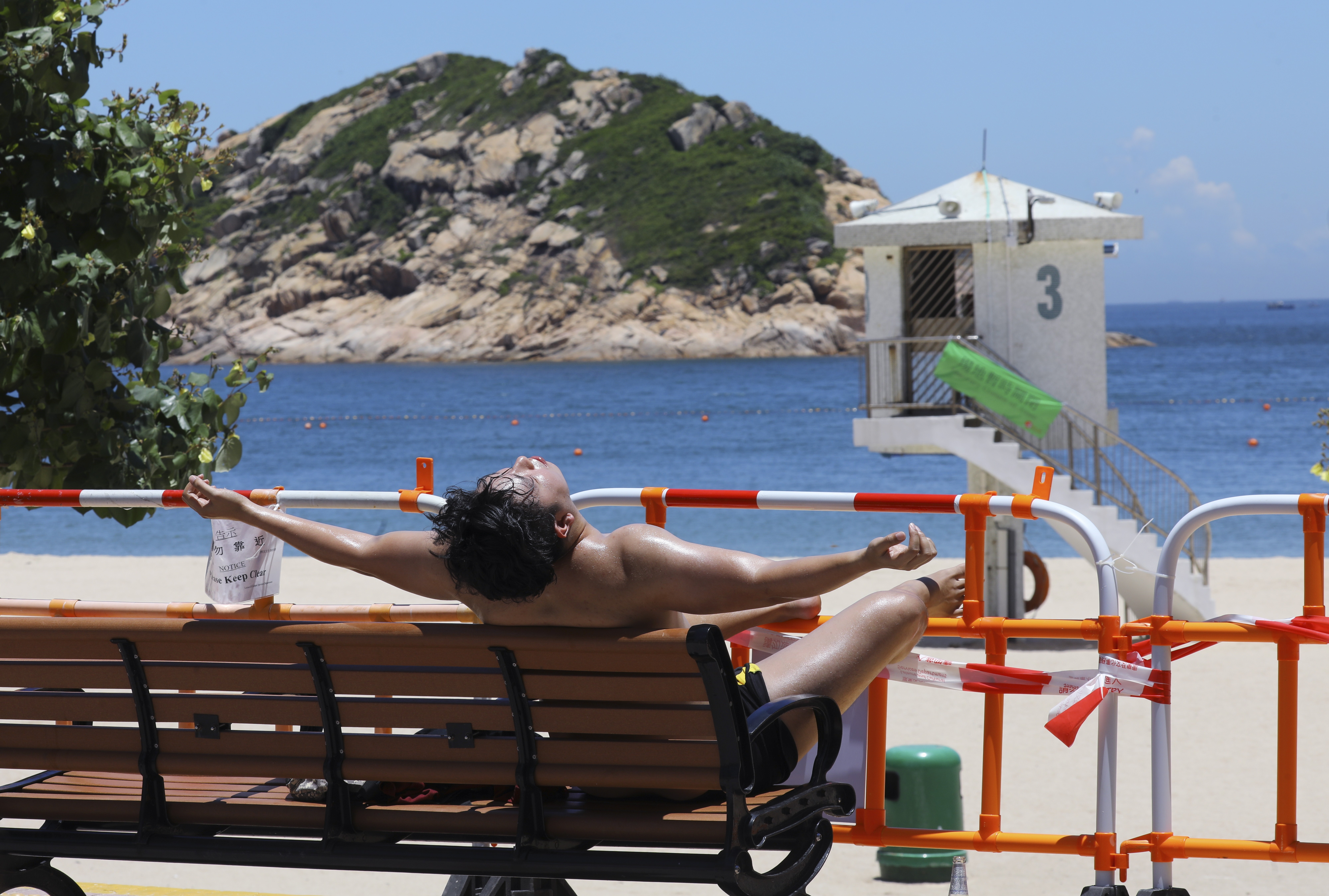 A man sunbathes behind the barricades at Shek O beach on July 26, days after Hong Kong’s beaches were closed. Photo: SCMP / Dickson Lee