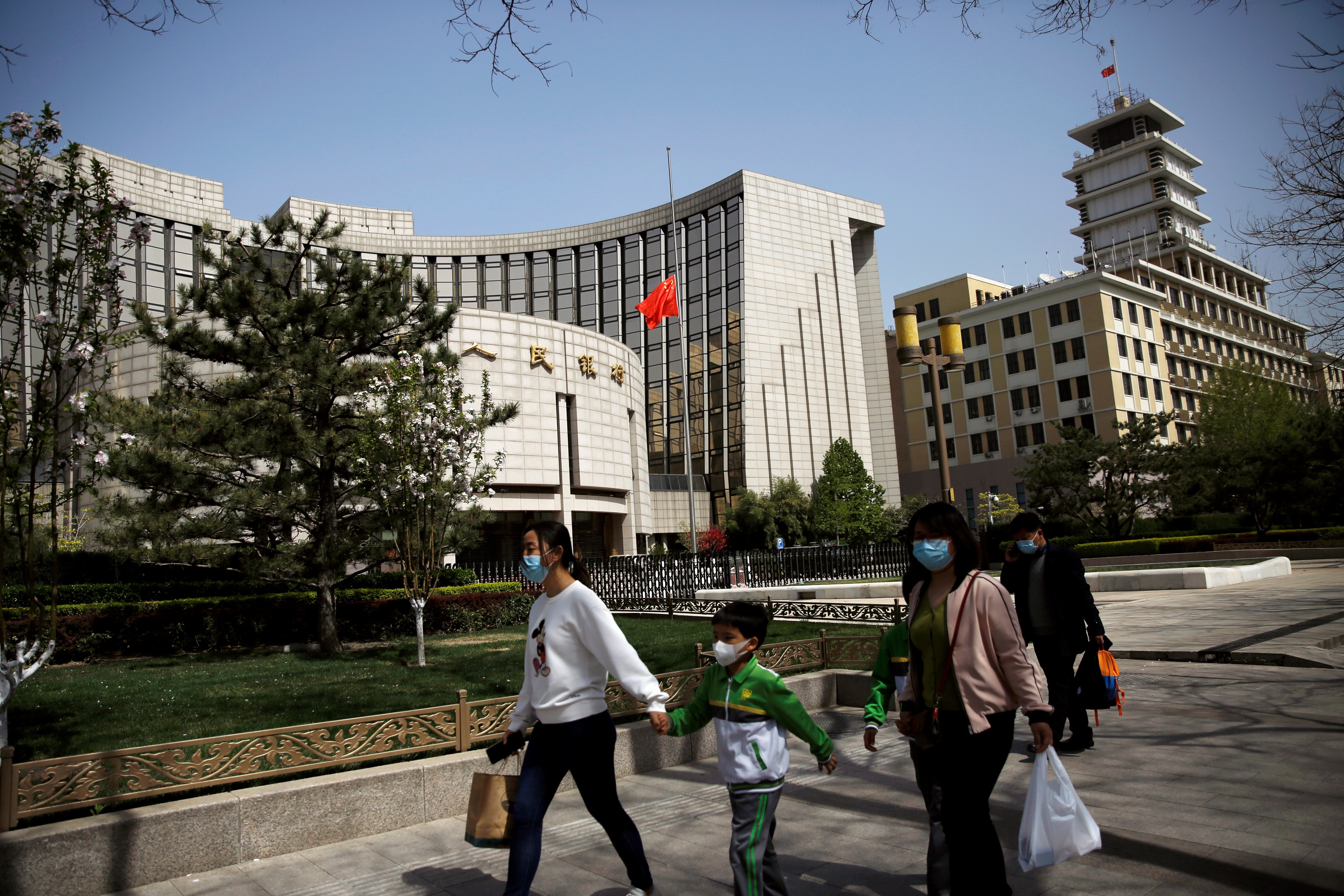 People wearing face masks walk past the headquarters of the People's Bank of China on April 4. The Chinese central bank’s conservative approach in its response to the economic impact of the Covid-19 pandemic could make it a darling for bond investors seeking higher yields. Photo: Reuters