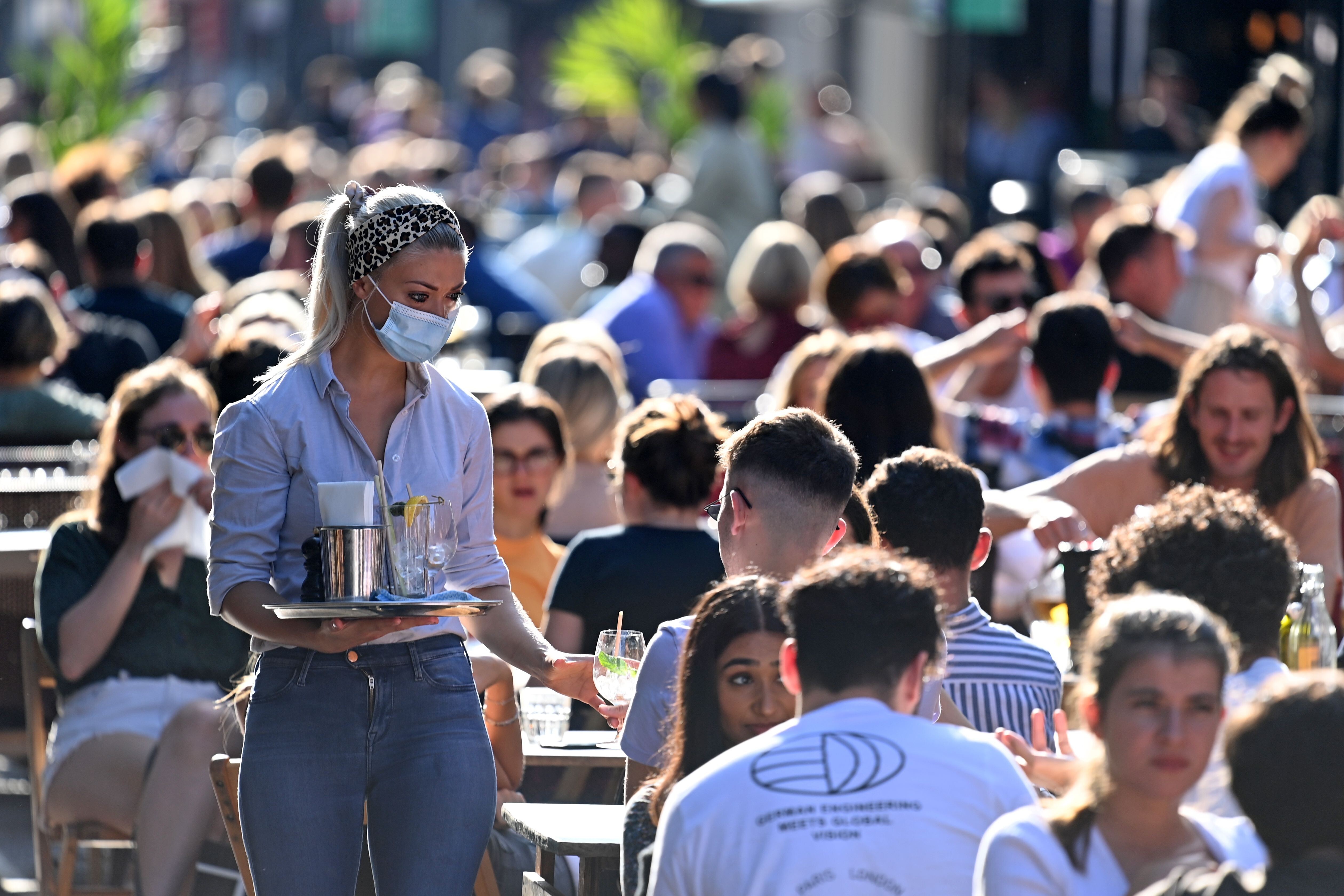 A waitress wearing a mask serves customers enjoying the summer sunshine at outdoor tables in Soho, central London, on September 20, as the British government considers fresh nationwide restrictions after an rise in Covid-19 cases. Photo: AFP