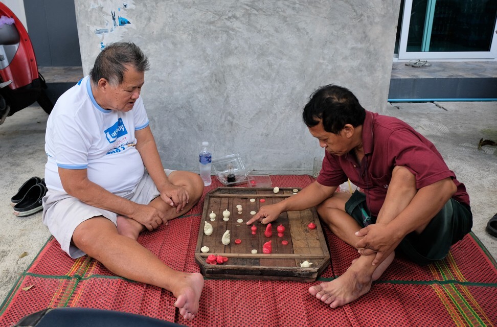 Two man play chess on the ground outside a house in Baan Khrua. Photo: Tibor Krausz