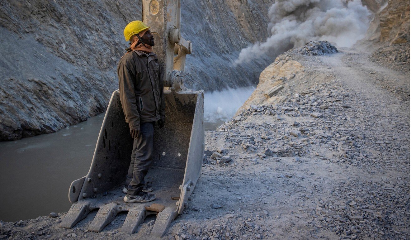 A worker from the Border Roads Organisation takes cover in an excavator bucket during a controlled explosion on a road under construction in Ladakh. Photo: Reuters