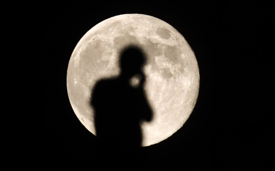 A person talking on a mobile phone is silhouetted against the full moon in Lhasa, in August 2012. Photo: Xinhua