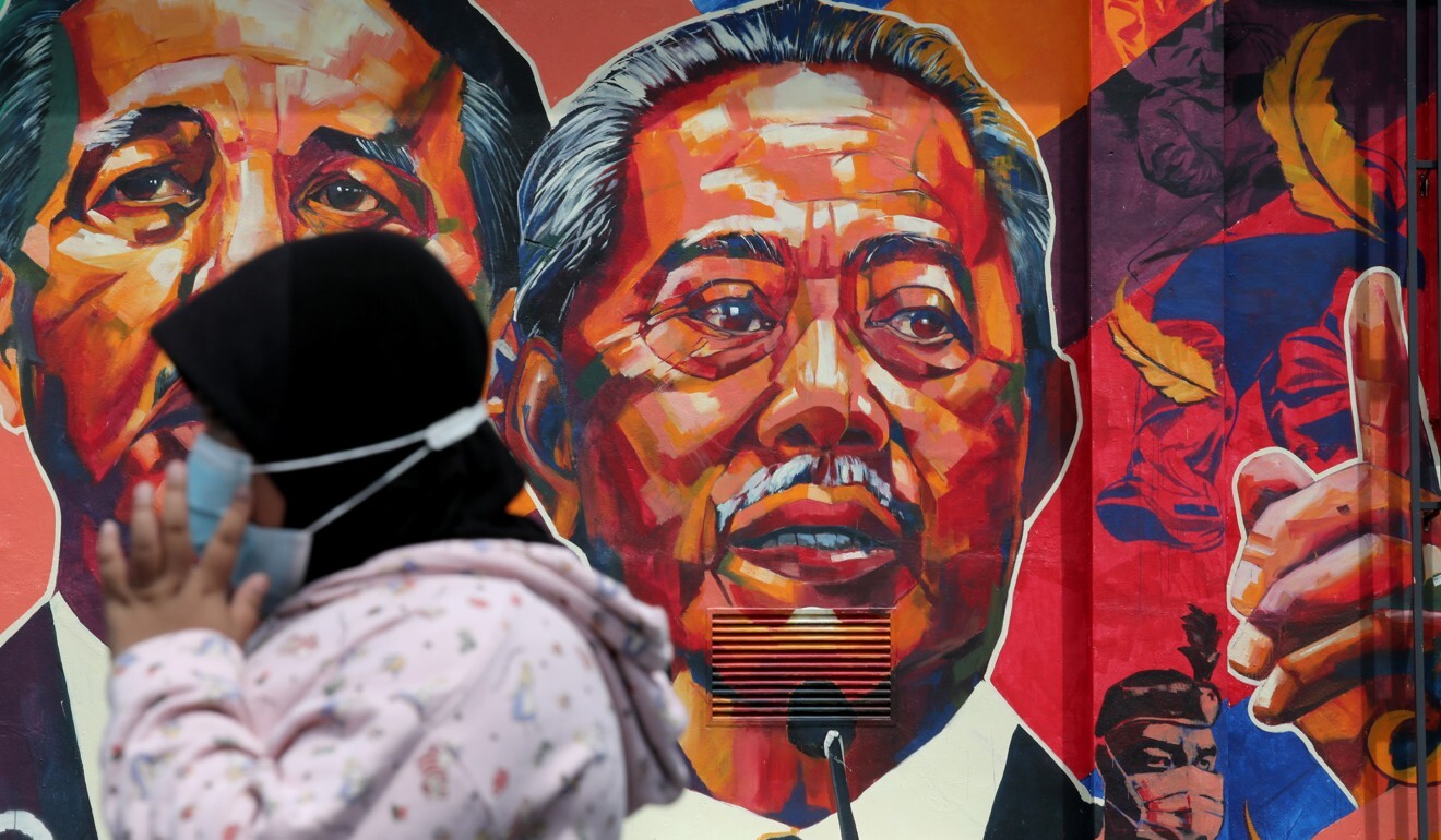 A woman passes by a mural depicting Malaysia's Prime Minister Muhyiddin Yassin, centre, in Kuala Lumpur. Photo: Reuters