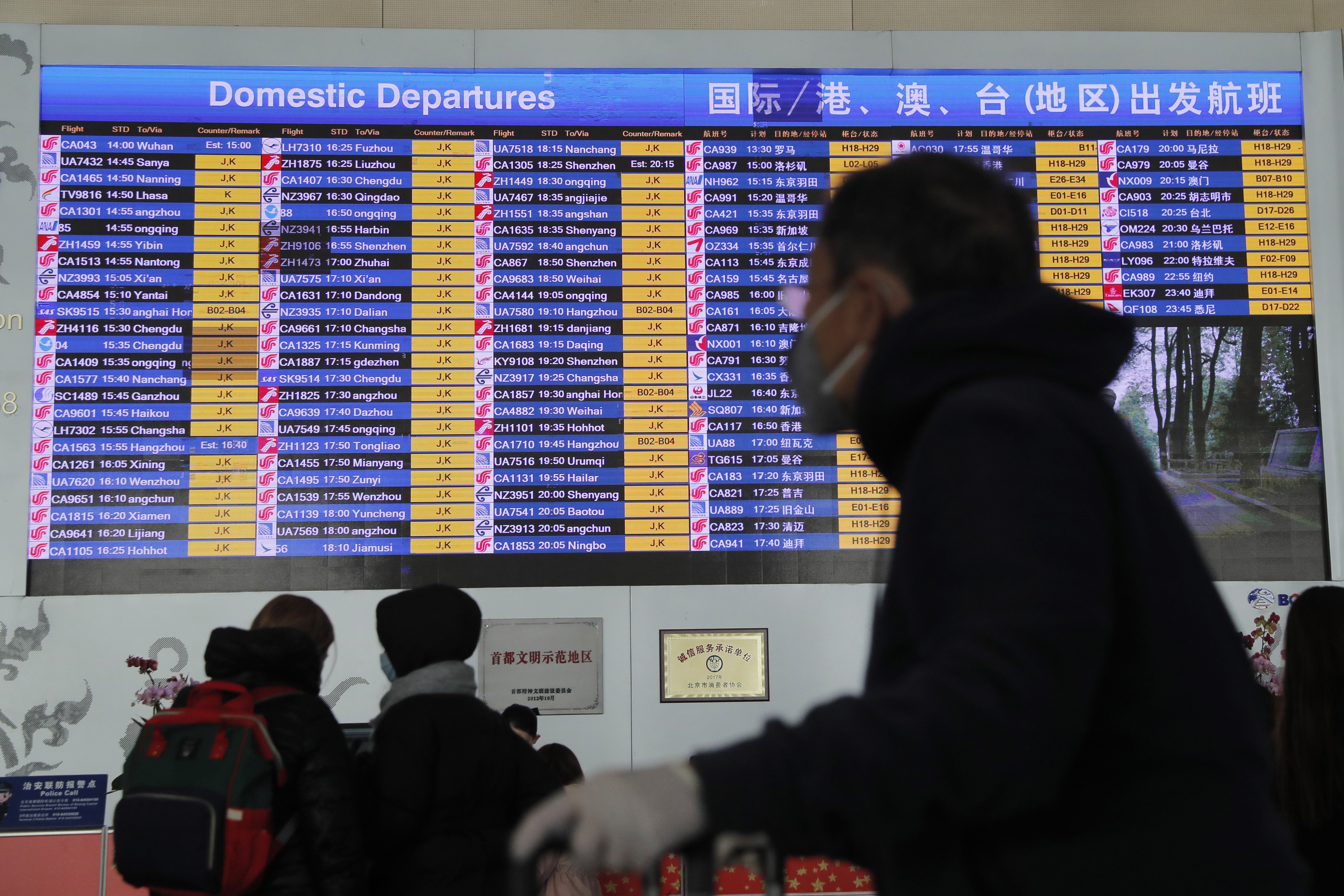 epa08165779 A passenger wears a mask passing by a departure information screen at terminal 3 of Beijing Capital International Airport in Beijing, China, 26 January 2020. Chinese official required all travel agencies to suspend the sale of all domestic and overseas group travel products due to coronavirus outbreak. EPA-EFE/WU HONG