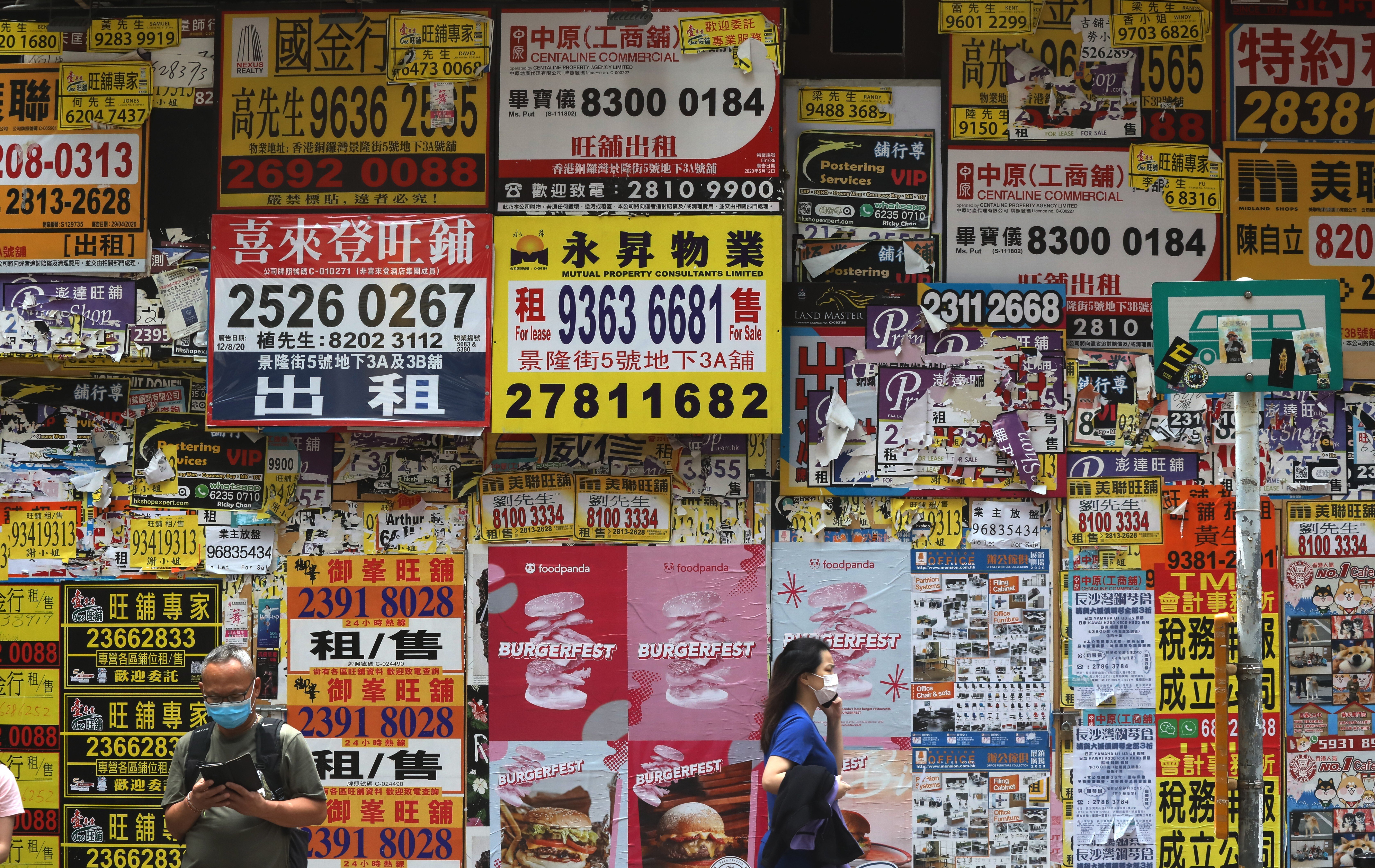 Pedestrians pass a store covered in posters for property agents in Causeway Bay, Hong Kong. Photo: K. Y. Cheng