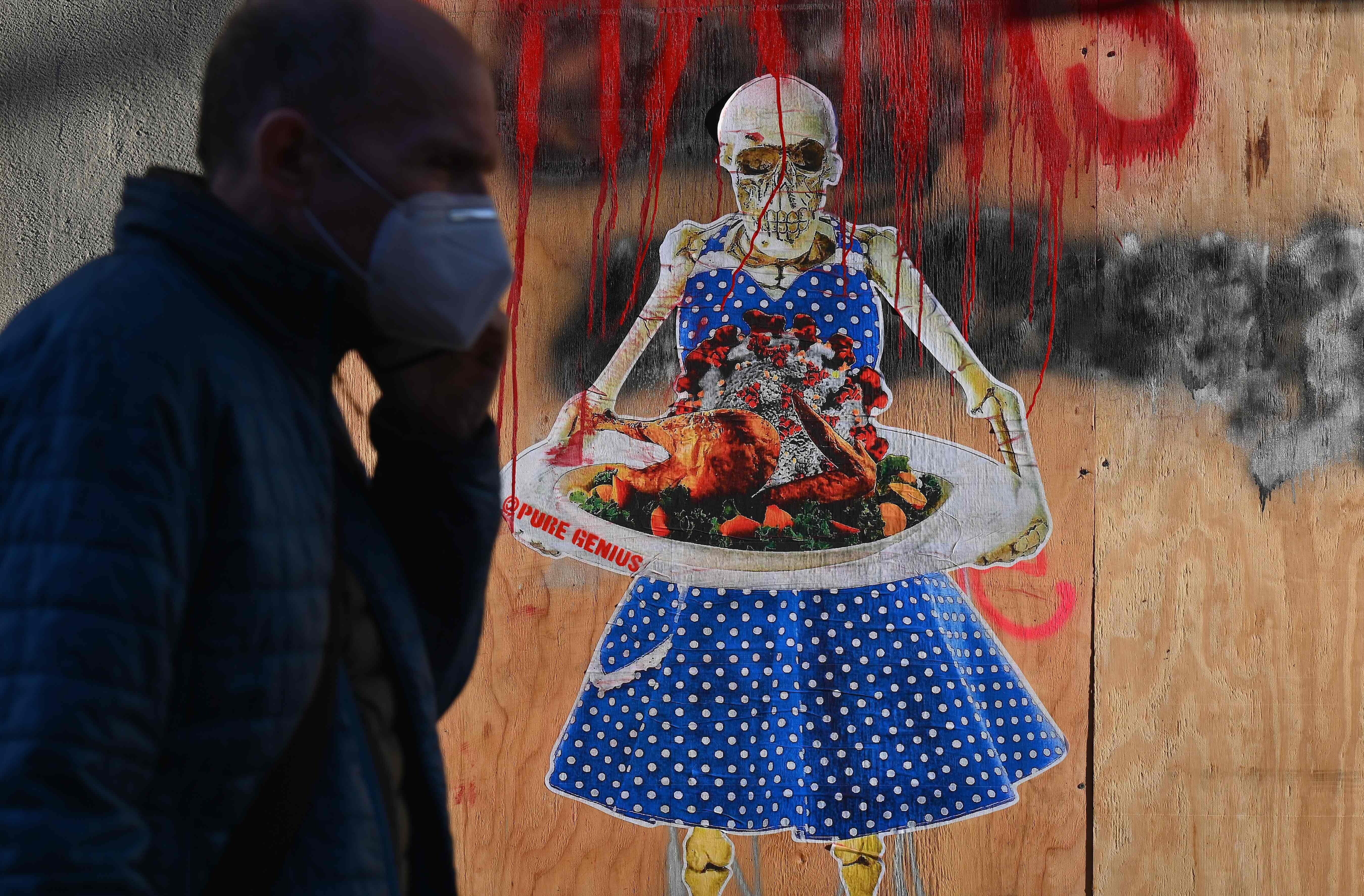 A man walks by street art by @puregenius in New York showing a skeleton holding a tray with a Thanksgiving turkey topped with coronavirus. Photo: AFP