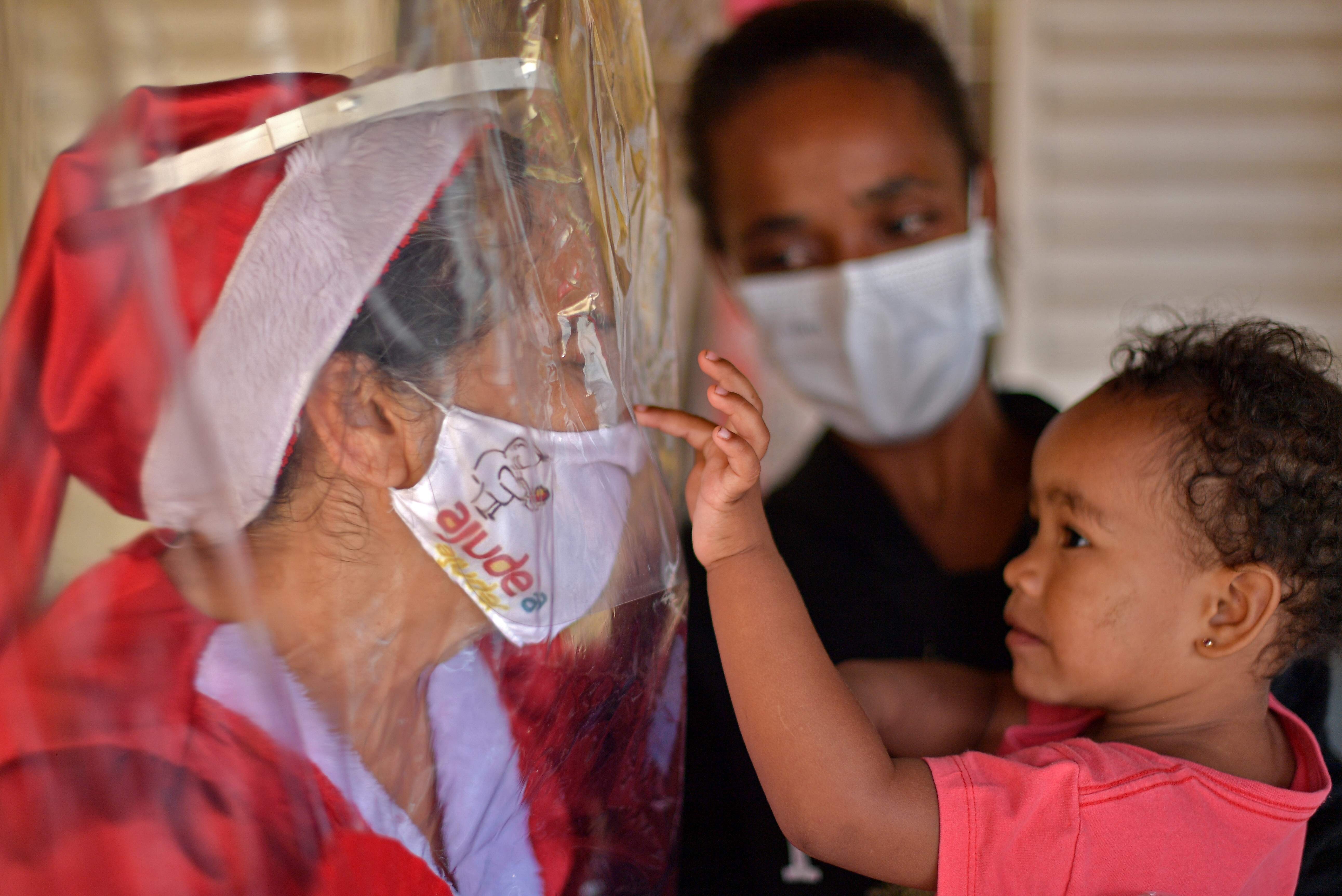 A child touches volunteer Fatima Sanson, dressed up as Mrs Claus, in Belo Horizonte, Minas Gerais state, Brazil, on December 7. Sanson delivers gifts and hugs to needy children every Christmas, but due to the coronavirus pandemic, this year she built an embrace curtain to allow children to touch her, keeping everyone safe. Photo: AFP