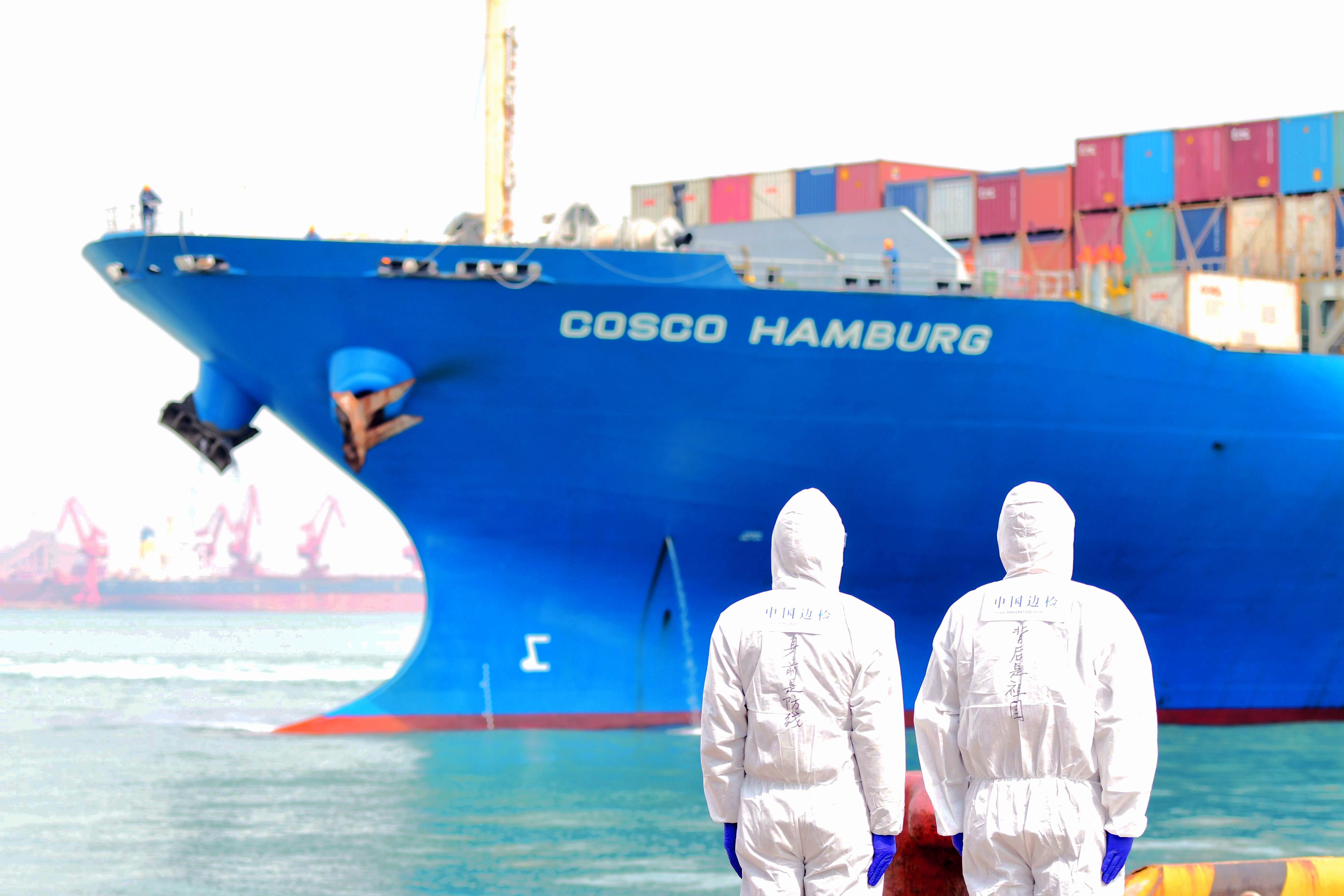 Port employees in protective suits watch a loaded container ship at Qingdao port in Shandong. China is the largest supply country for seafarers, so the vaccination of the Chinese maritime workforce will become an acute public health issue. Photo: DPA