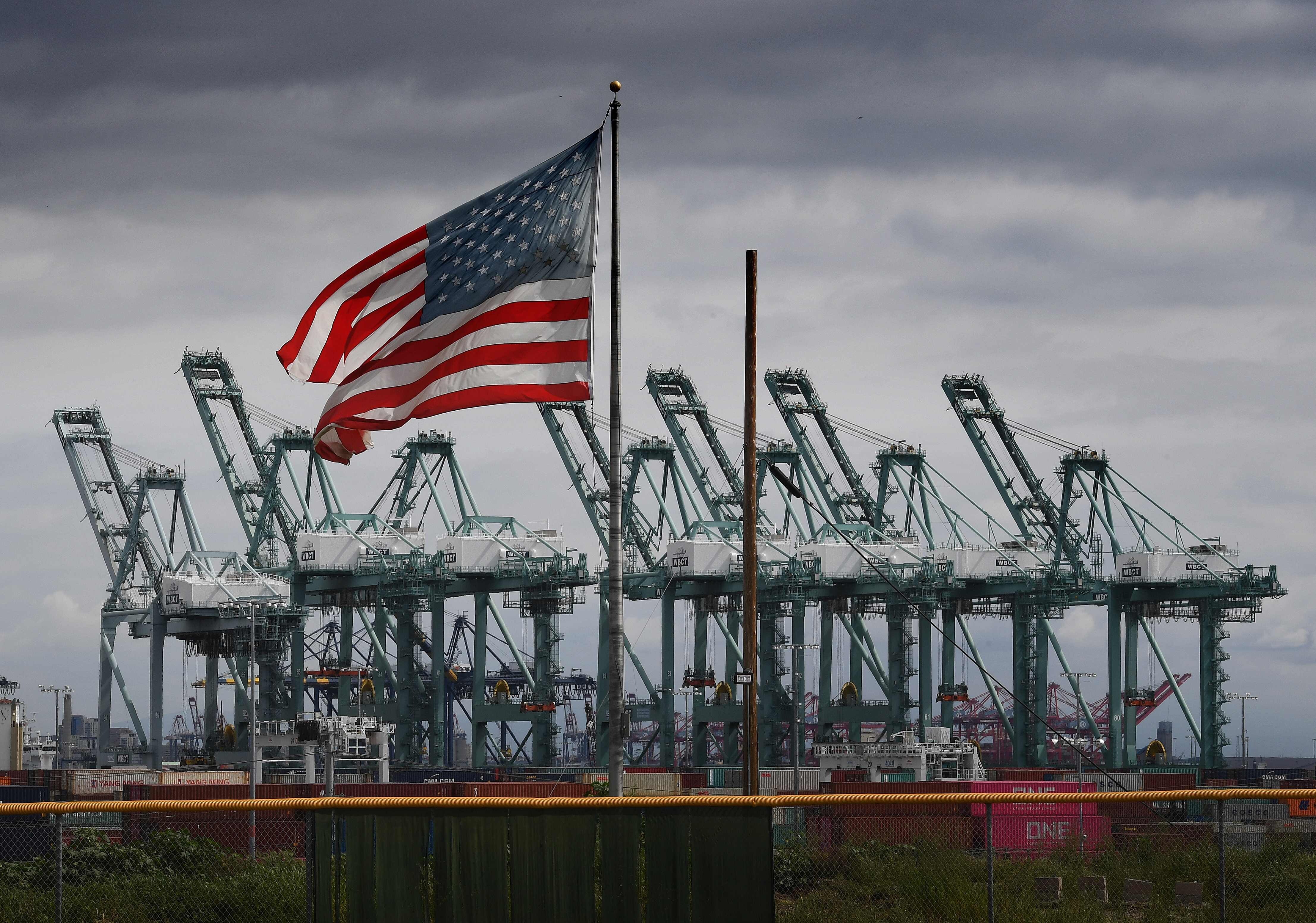 The US flag flies over shipping cranes and containers in Long Beach, California, on March 4, 2019. Photo: AFP