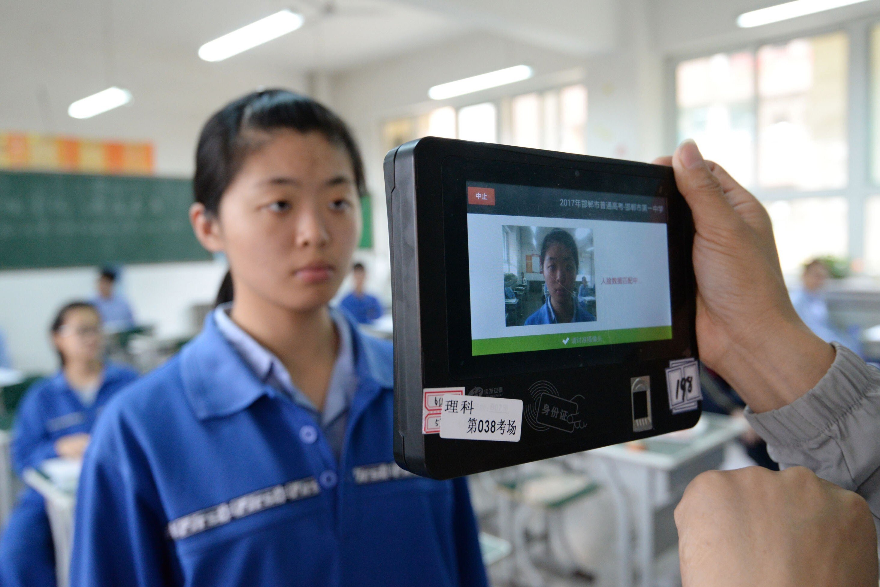 A teacher uses a machine which employs both fingerprint and facial recognition technology to check the identification of a student before a simulated college entrance exam in Handan in China‘s northern Hebei province on June 6, 2017. Photo: STR/AFP via Getty