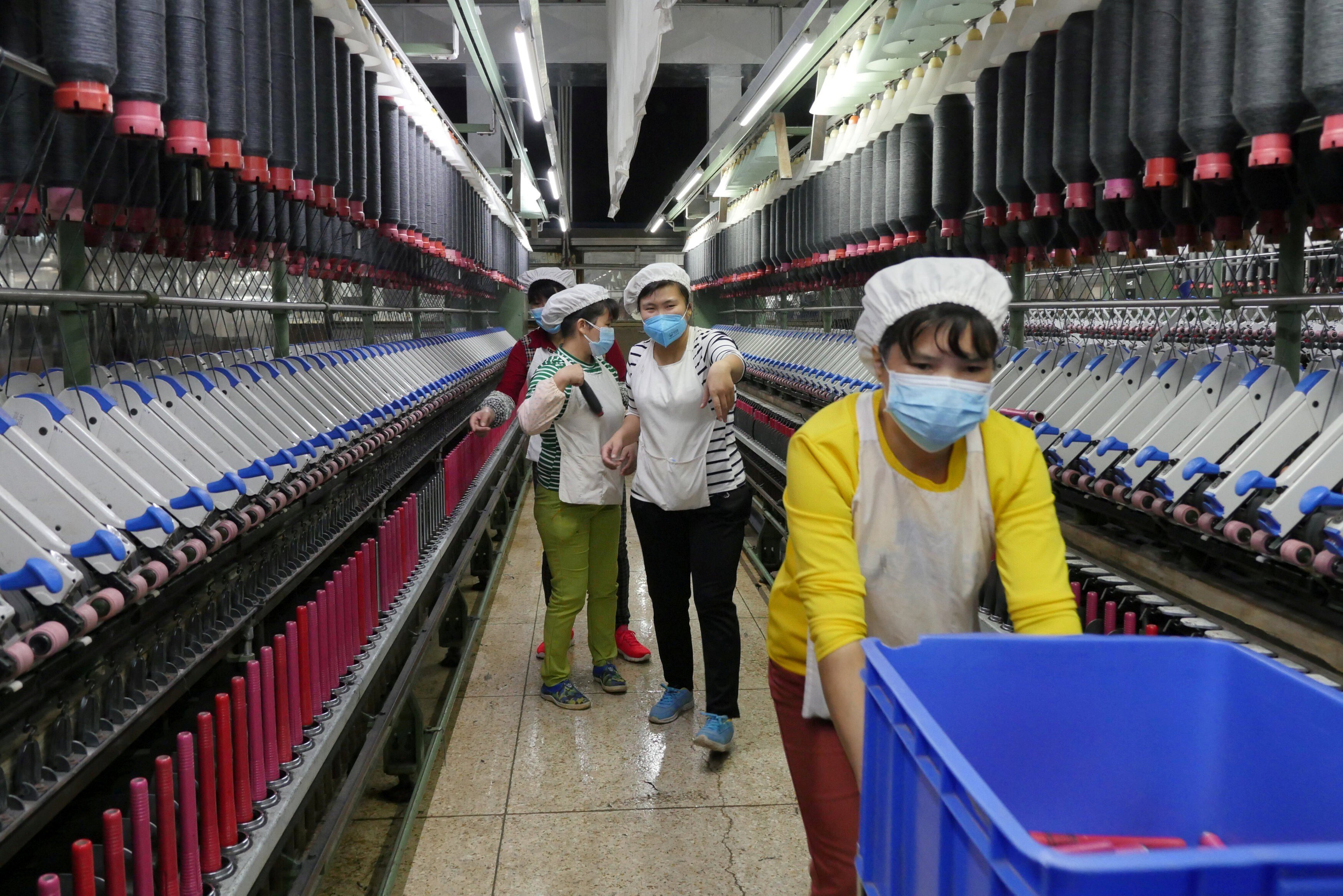 A worker beckons to her colleague as she rolls away carts of unused tools between rows of spinning machine at a factory owned by Hong Kong’s Novetex Textiles Limited in Zhuhai, Guangdong province, on December 13, 2016. Photo: Reuters